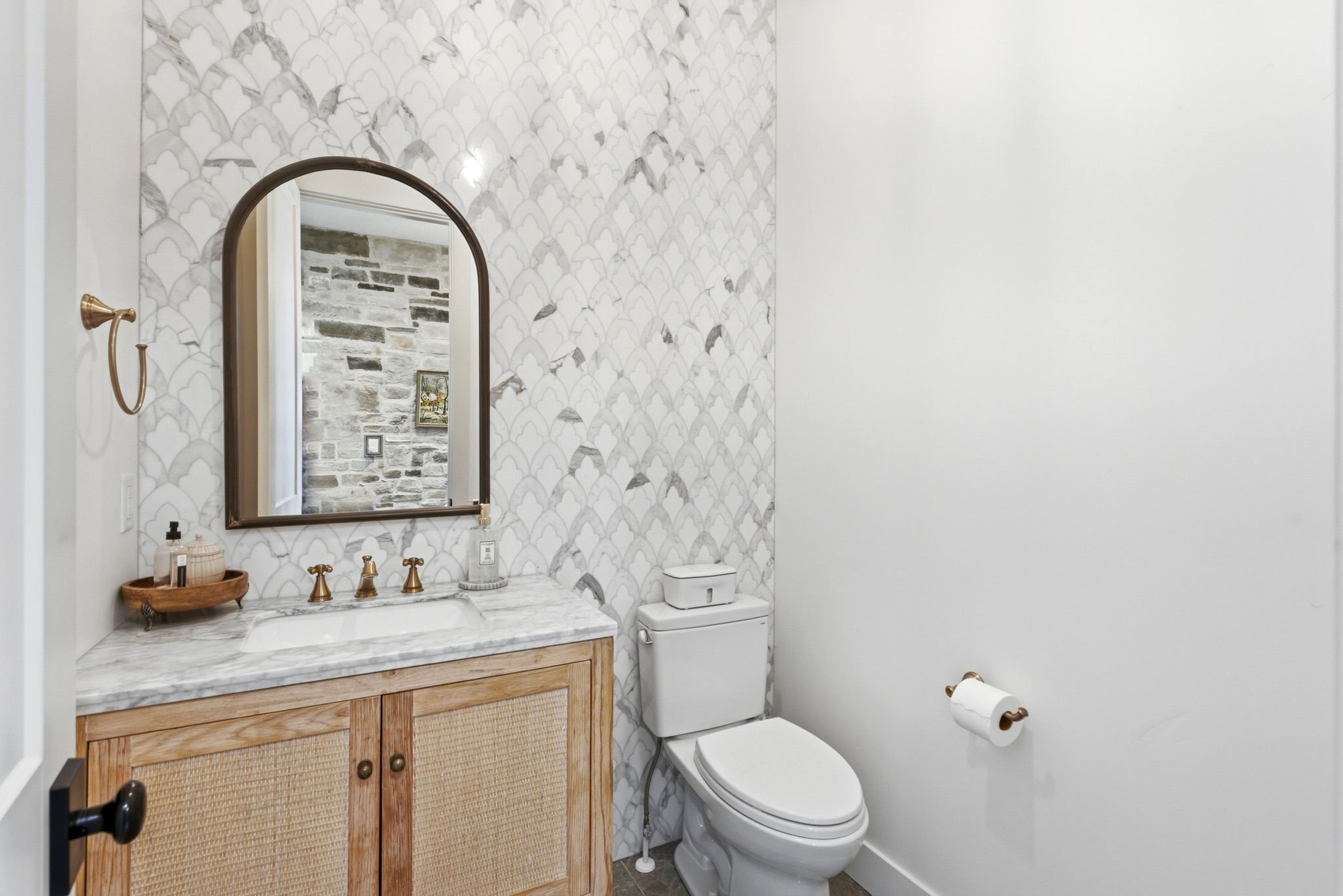 Powder room featuring a natural wood vanity with rattan cabinet fronts, a white stone countertop, and an arched mirror
