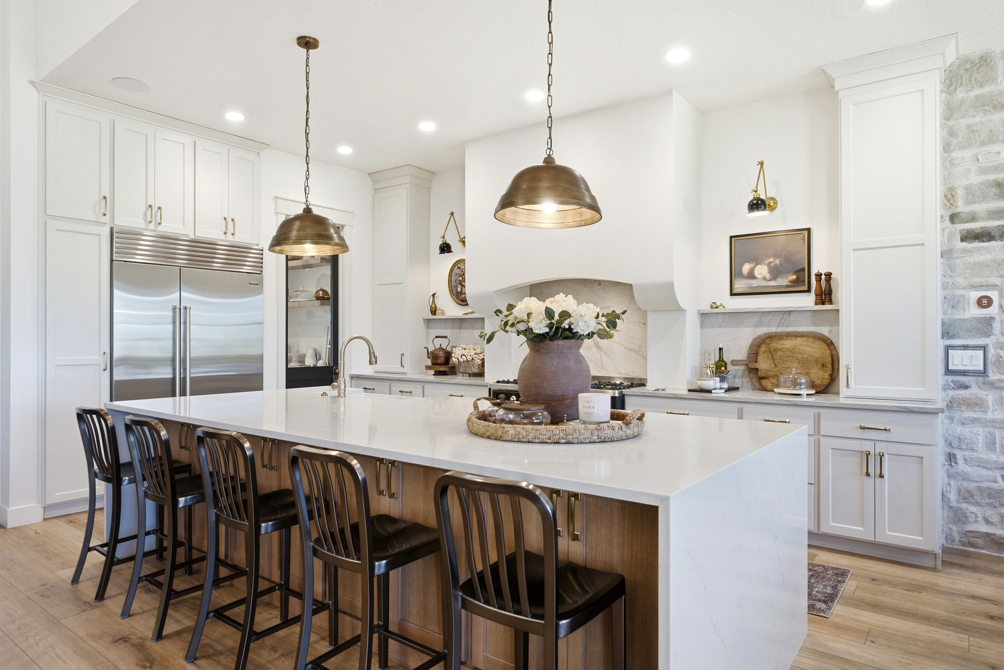 Contemporary kitchen featuring a large central island with seating, stainless steel appliances, white cabinetry, wood-finish flooring, and a stone accent wall