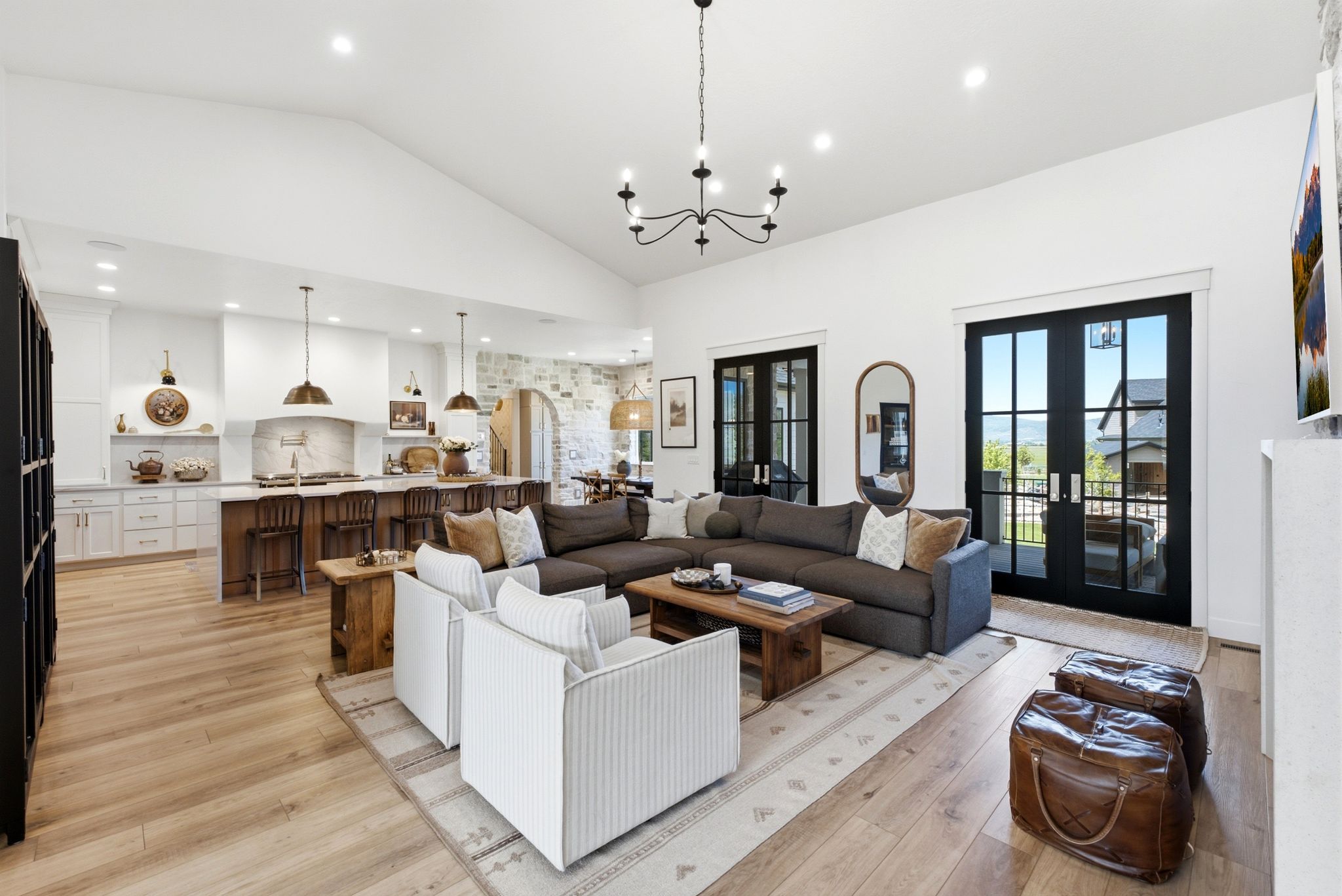 Open-concept living space featuring vaulted ceilings, light wood-finish flooring, a kitchen island with seating, and black-framed glass doors