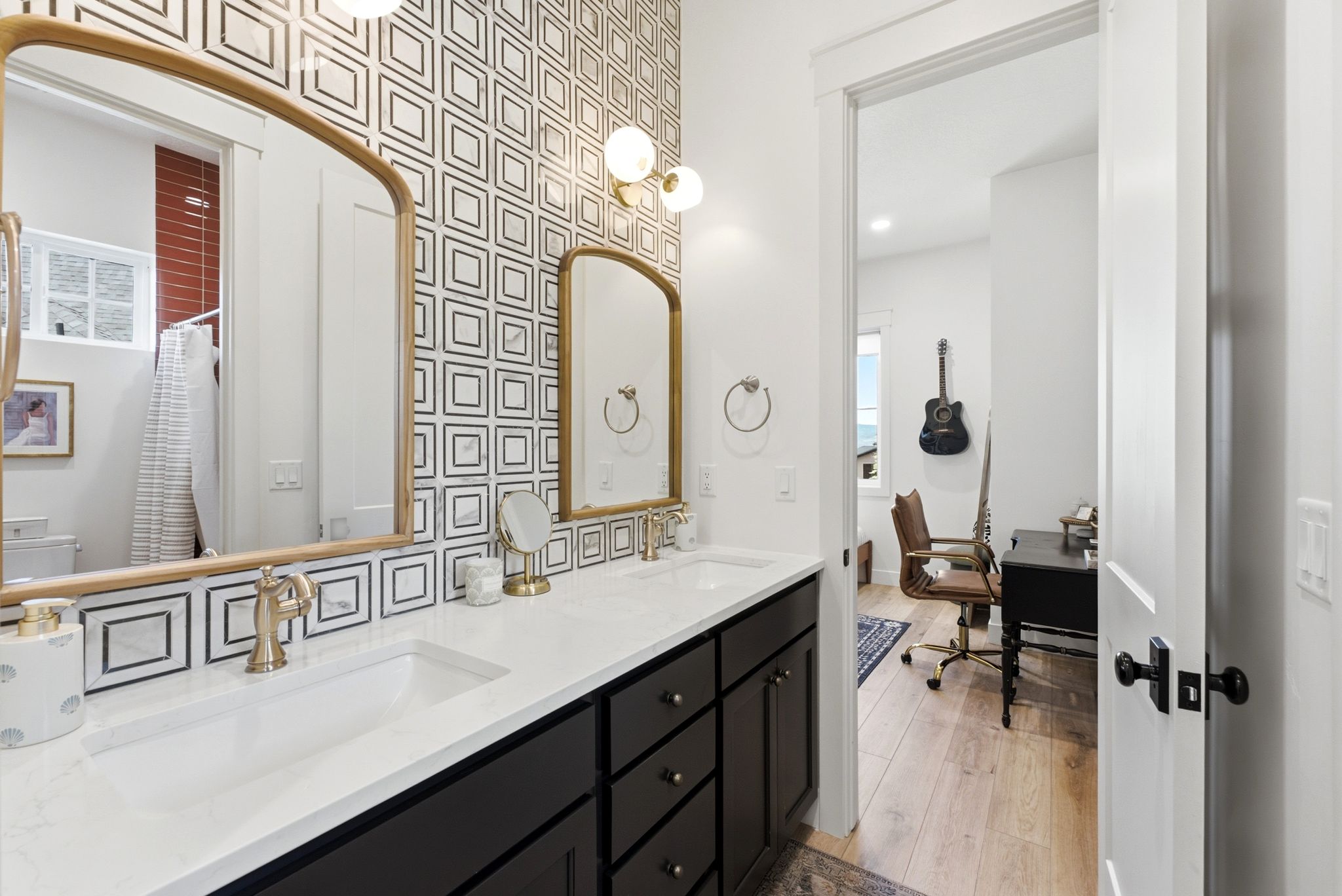 Dual vanity with integrated sinks, brushed gold fixtures, black cabinetry, and a geometric pattern accent wall