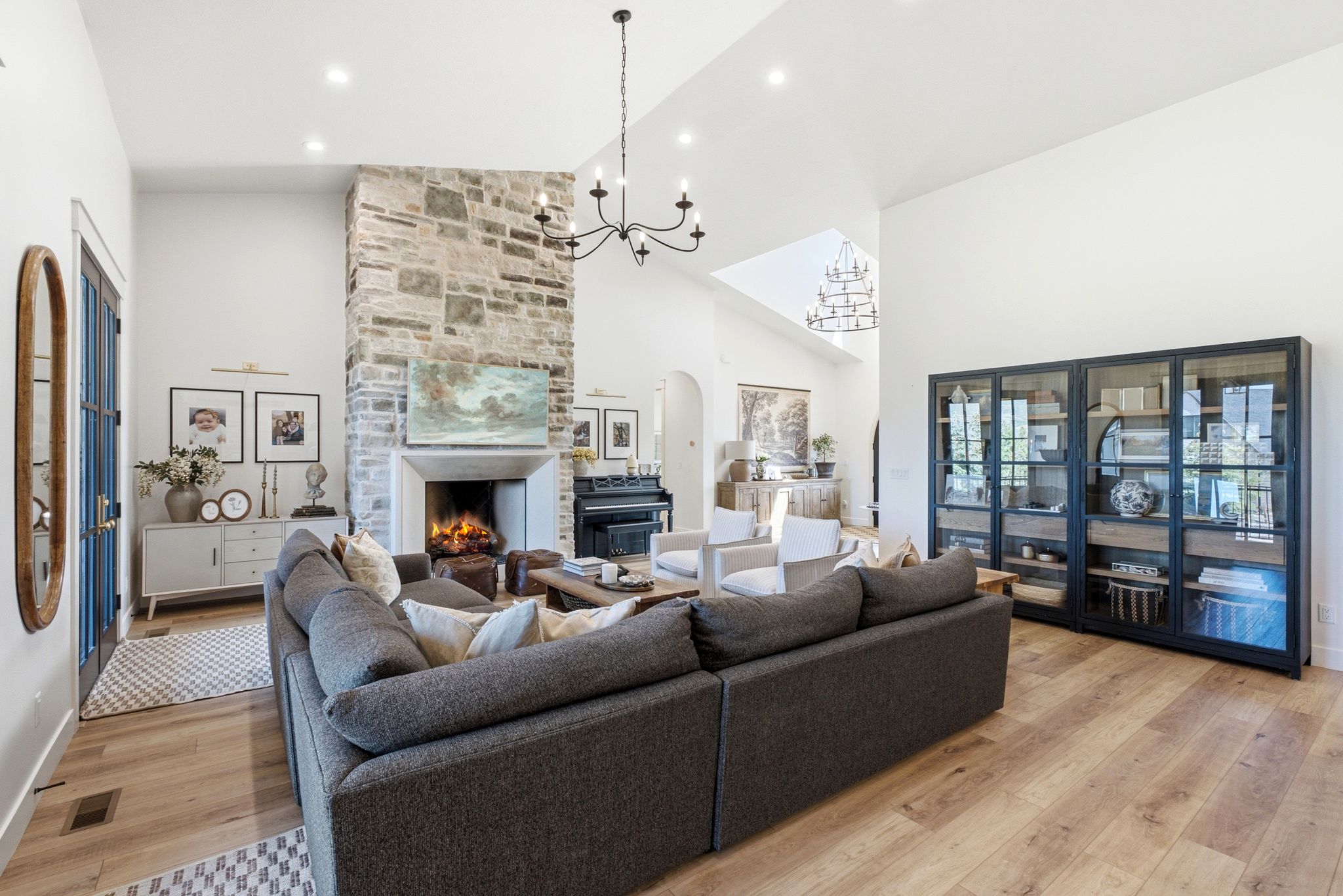 Spacious living area featuring a floor-to-ceiling stone fireplace with a substantial mantel, vaulted ceilings, and wood-finish flooring
