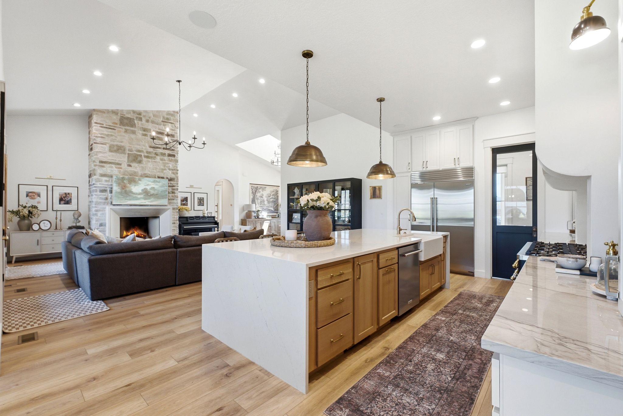 Gourmet kitchen featuring a large central island with light wood-finish cabinetry and a farmhouse sink, stainless steel appliances, and ceiling-mounted pendant lighting
