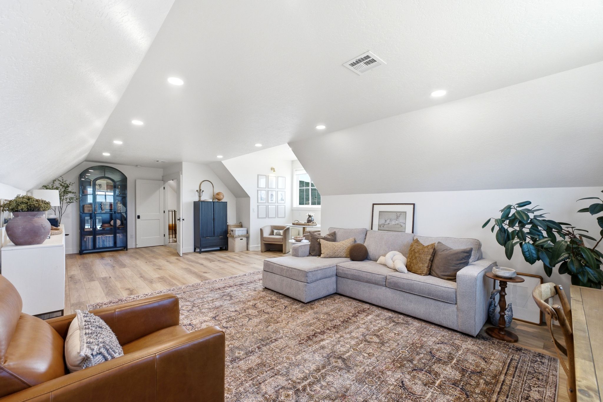Spacious loft area featuring light wood-finish flooring, recessed lighting, and a white vaulted ceiling