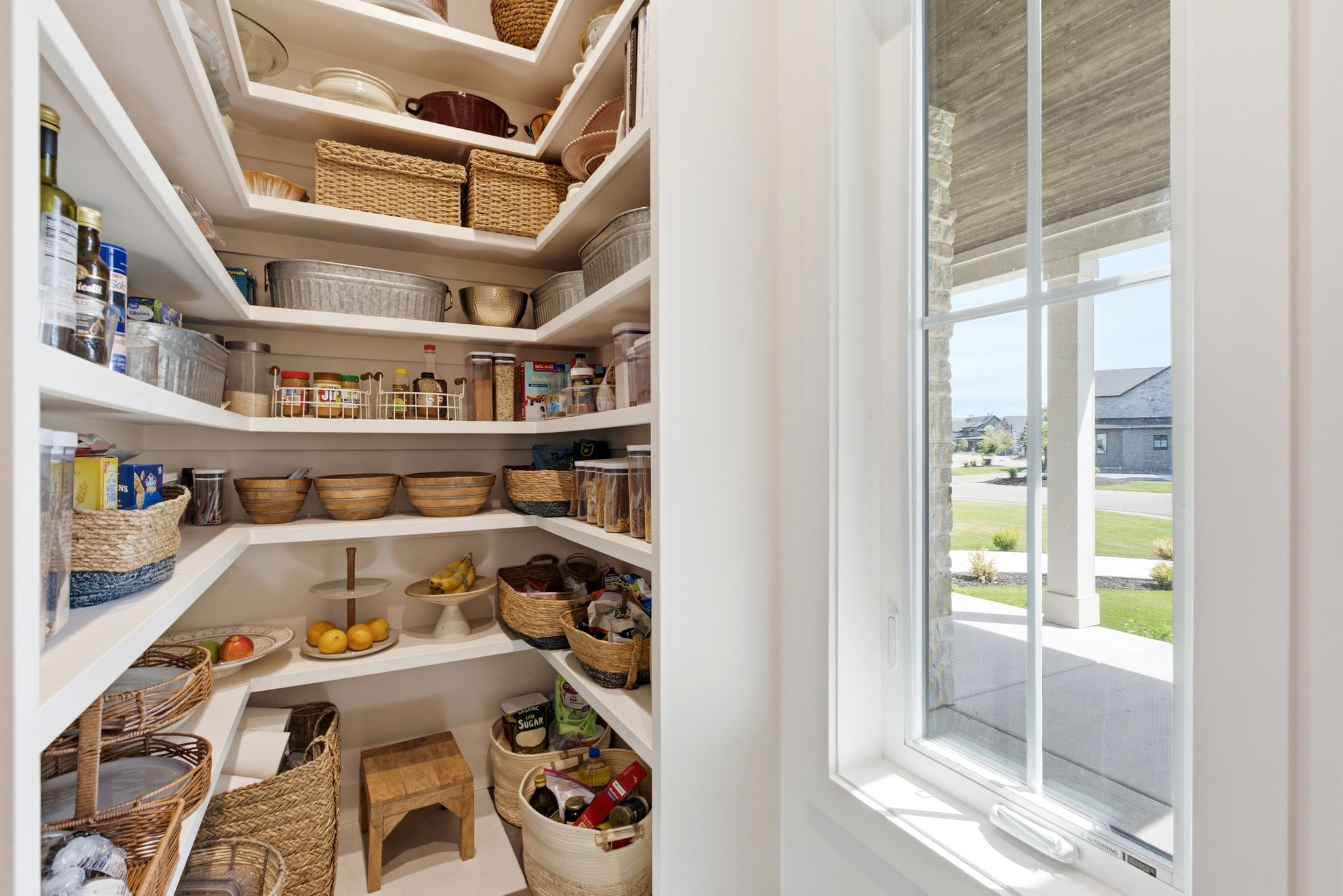 Walk-in pantry featuring extensive built-in shelving, white finishes, and a single-pane window with white muntins