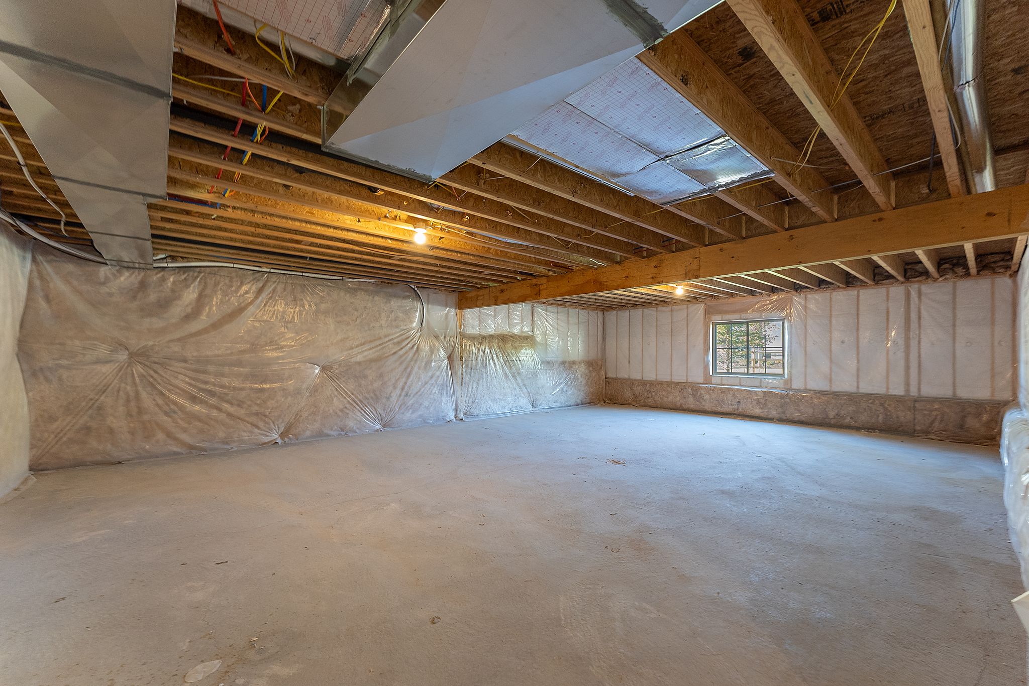 Unfinished basement featuring exposed wood joists, concrete flooring, insulated walls, and a window providing natural light