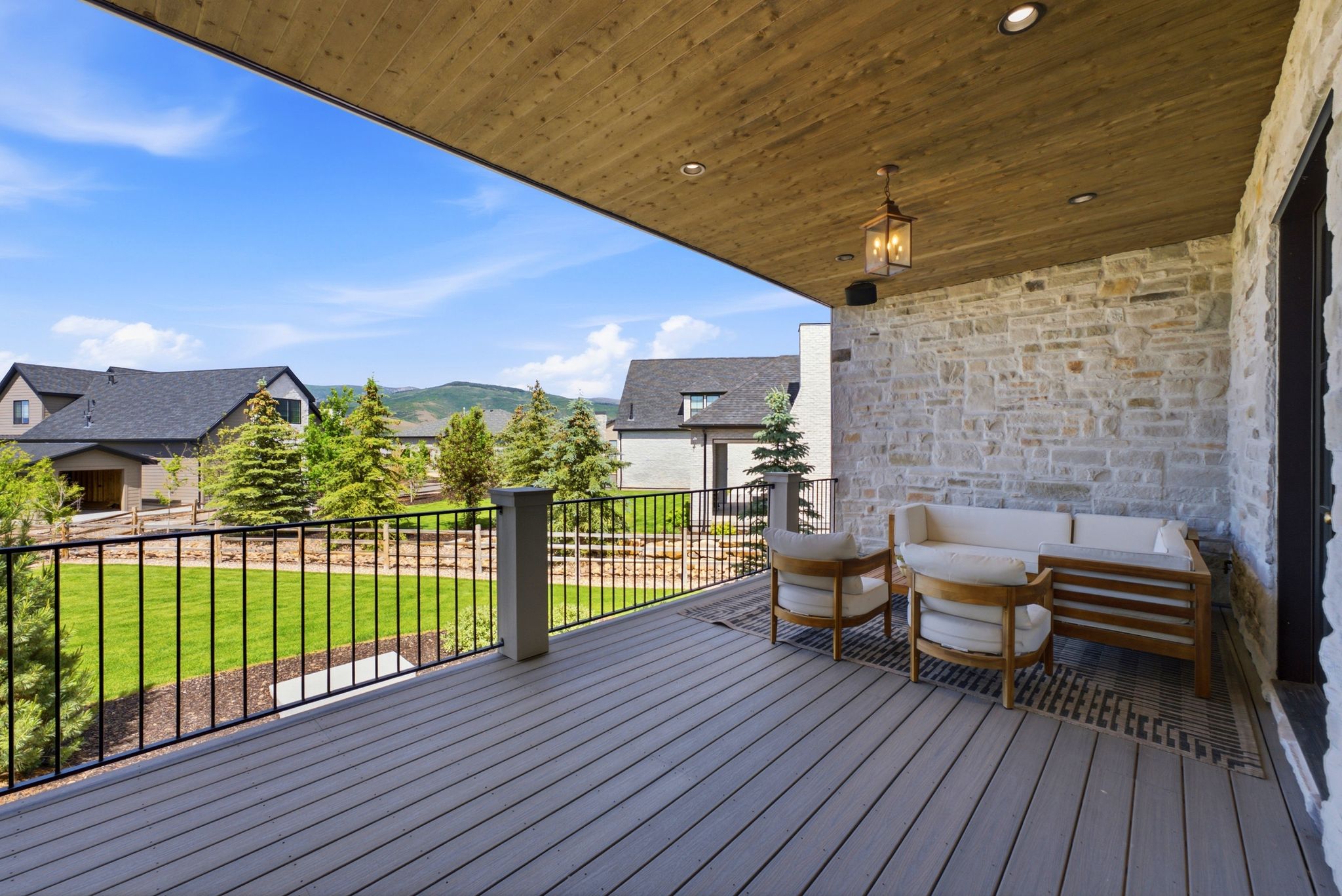 Expansive covered deck featuring composite decking, a stone accent wall, and a wood-paneled ceiling with recessed lighting