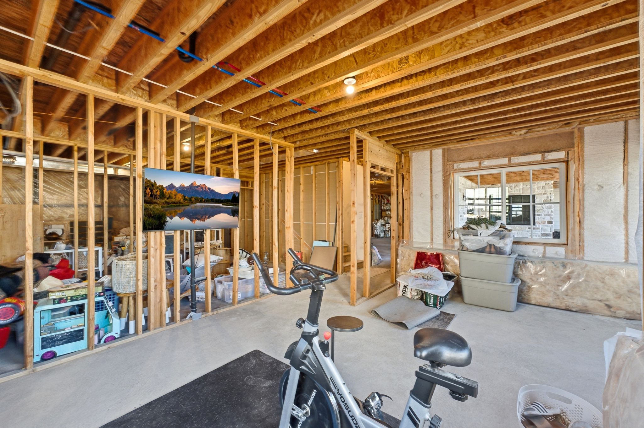 Unfinished basement featuring exposed wood joists and framing, concrete flooring, and a large window