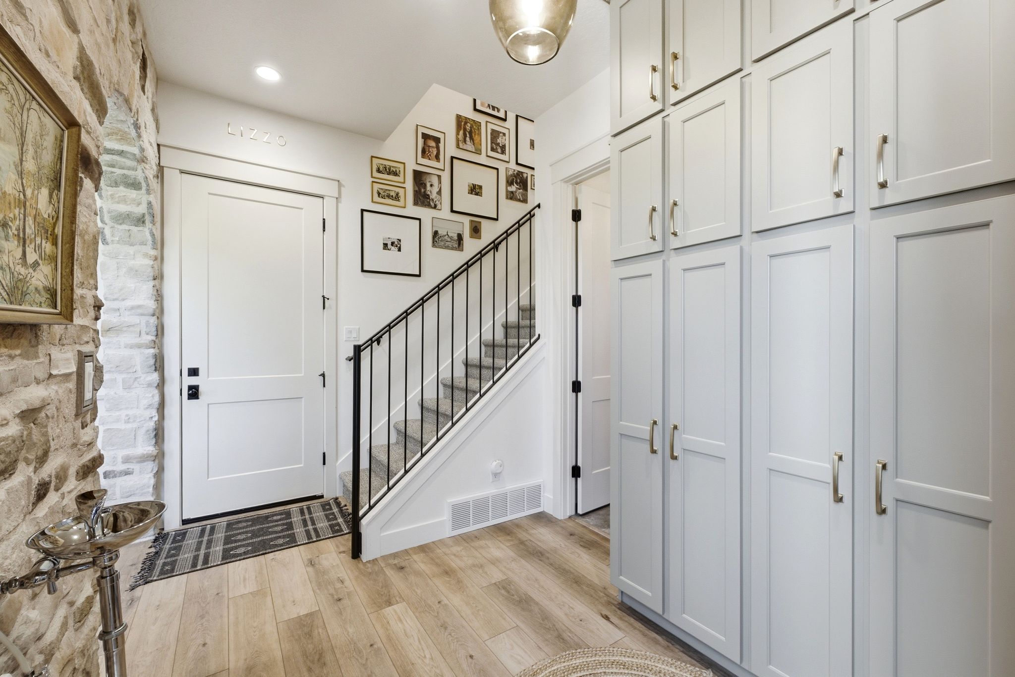 Entryway featuring extensive built-in cabinetry, wood-finish flooring, a stone accent wall, a white paneled door, and a staircase with a black metal railing