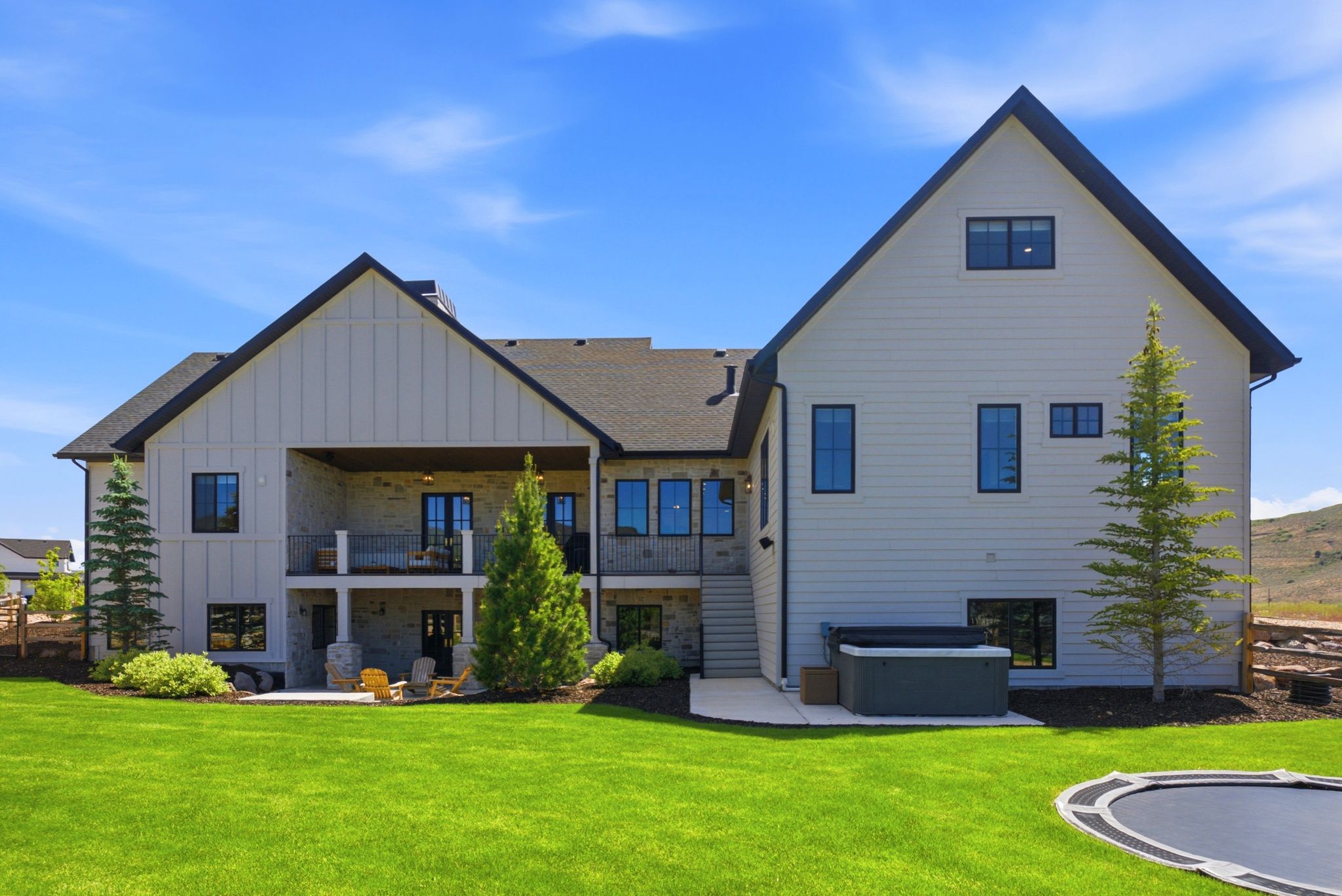 Rear exterior featuring a covered deck, lower patio, and a stone facade