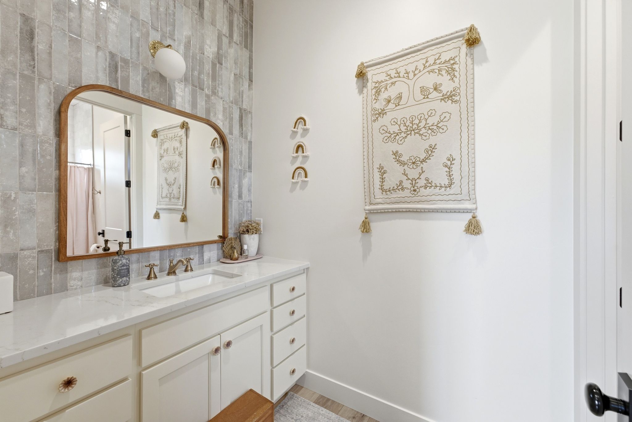 Bathroom vanity with a white countertop and integrated sink, featuring a wood-frame mirror and a tiled accent wall