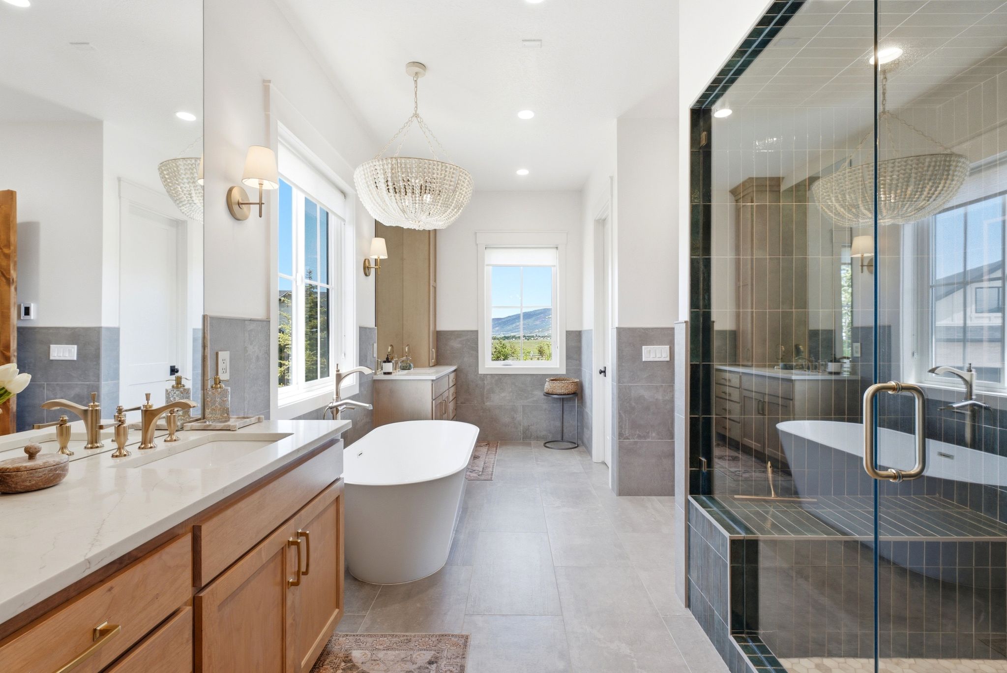Spacious bathroom featuring a freestanding soaking tub, a large walk-in glass-enclosed shower, a double vanity with stone countertop, and two ornate chandeliers