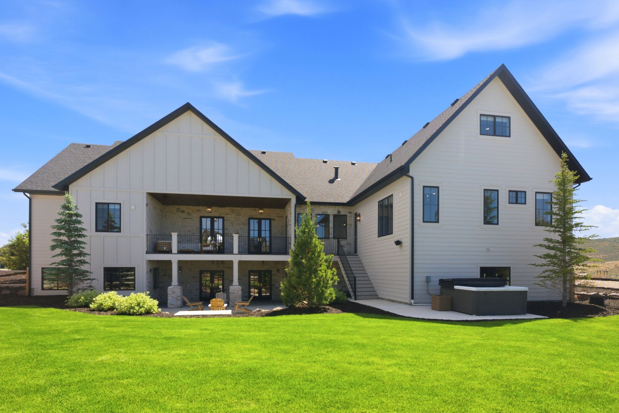 Contemporary farmhouse exterior featuring board and batten siding, black-framed windows, a covered upper balcony, and a ground-level patio