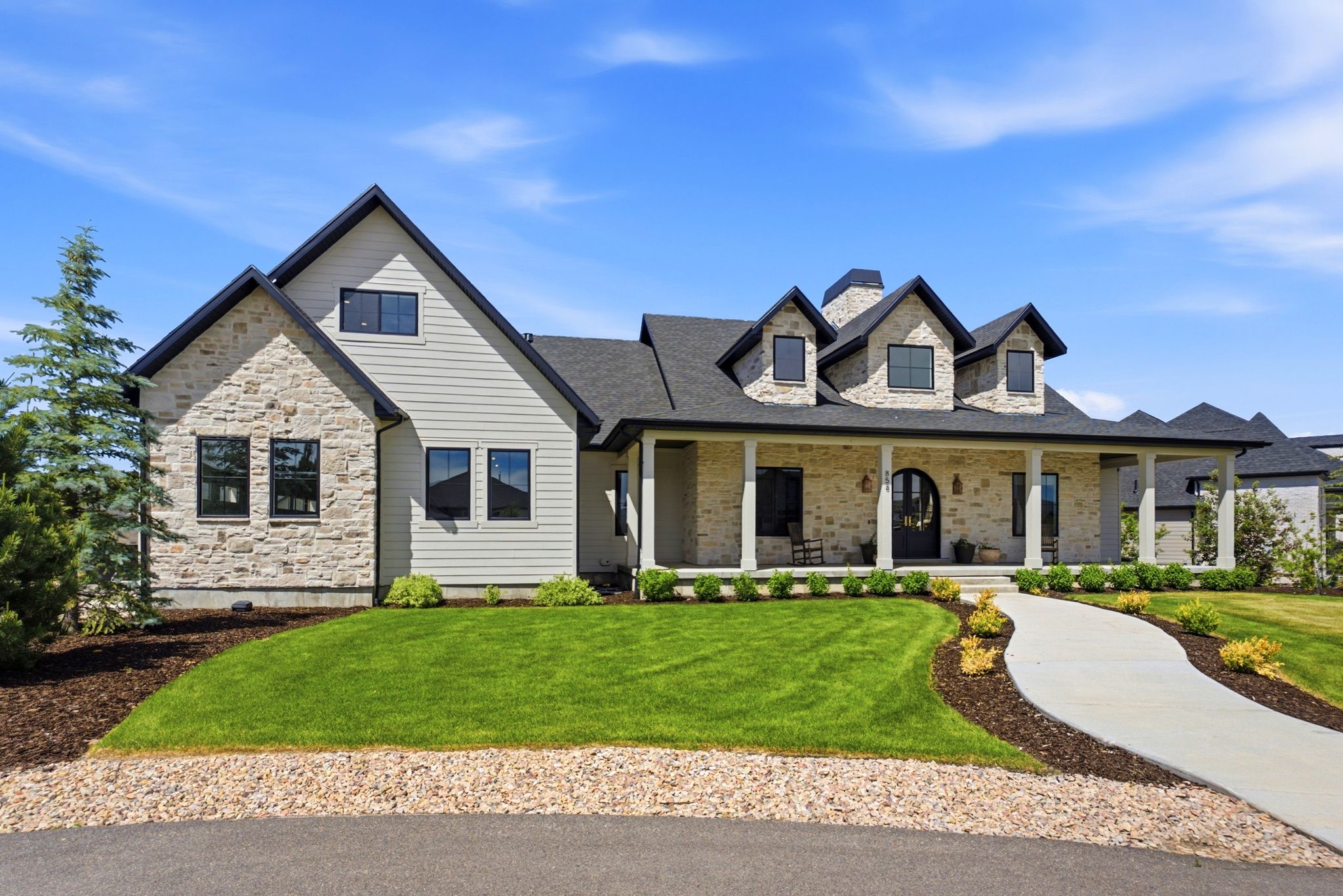 Stone and siding exterior with dark-framed windows, a covered front porch, and dormer windows