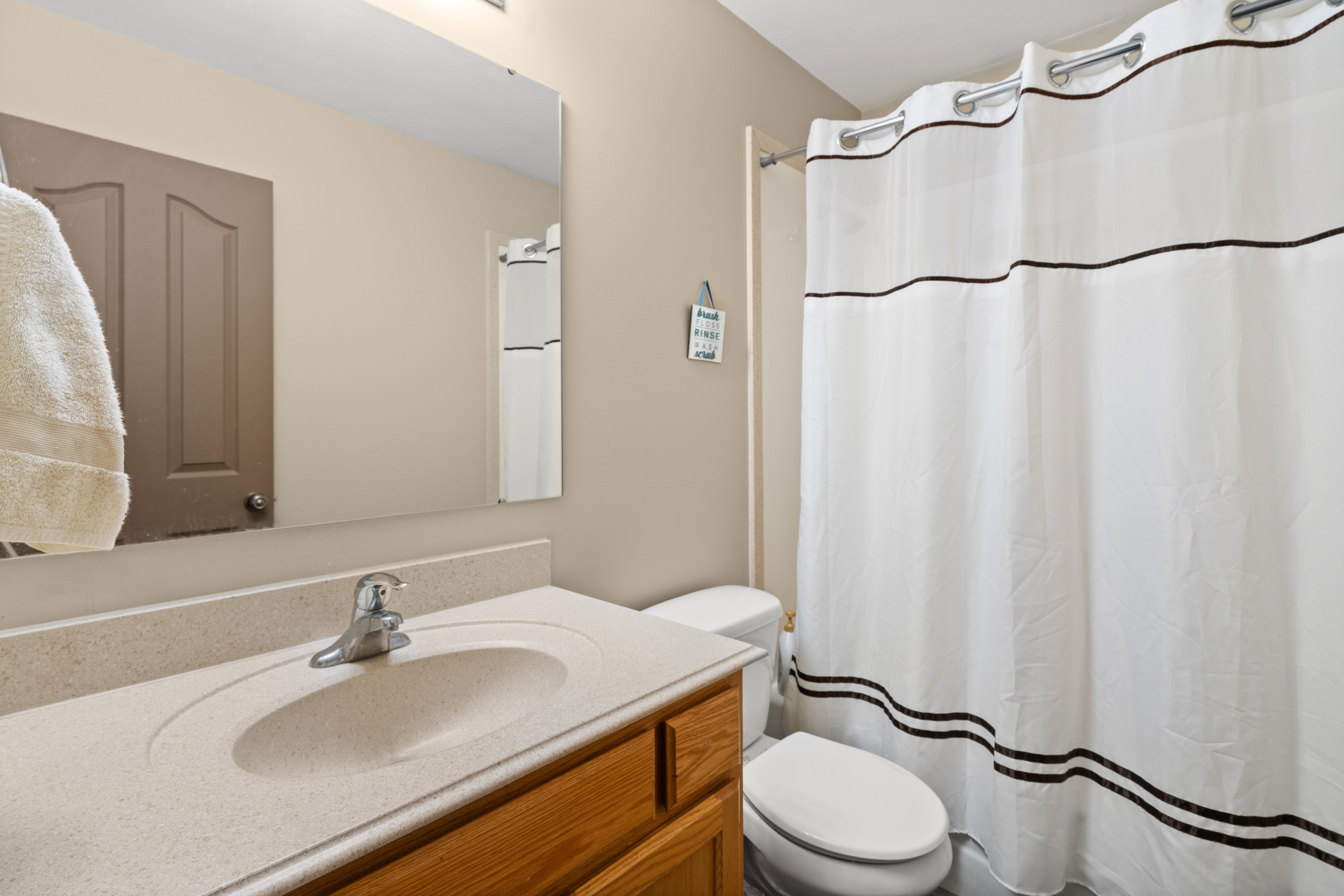 Bathroom featuring a single vanity with an integrated sink, a large wall-mounted mirror, and a white shower curtain with dark banding