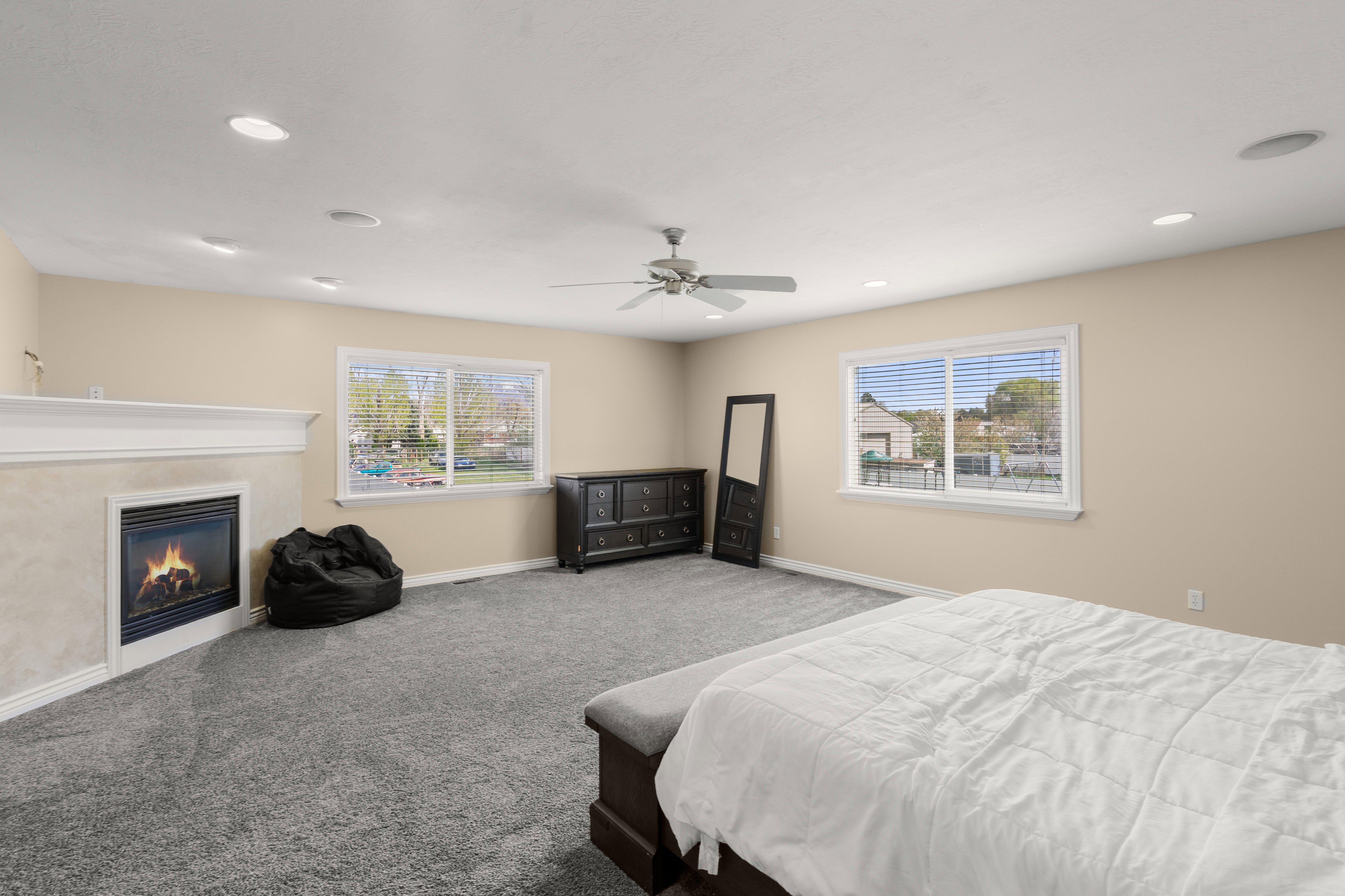 Spacious room featuring a fireplace with a white mantel, recessed lighting, a ceiling fan, and two large windows with blinds