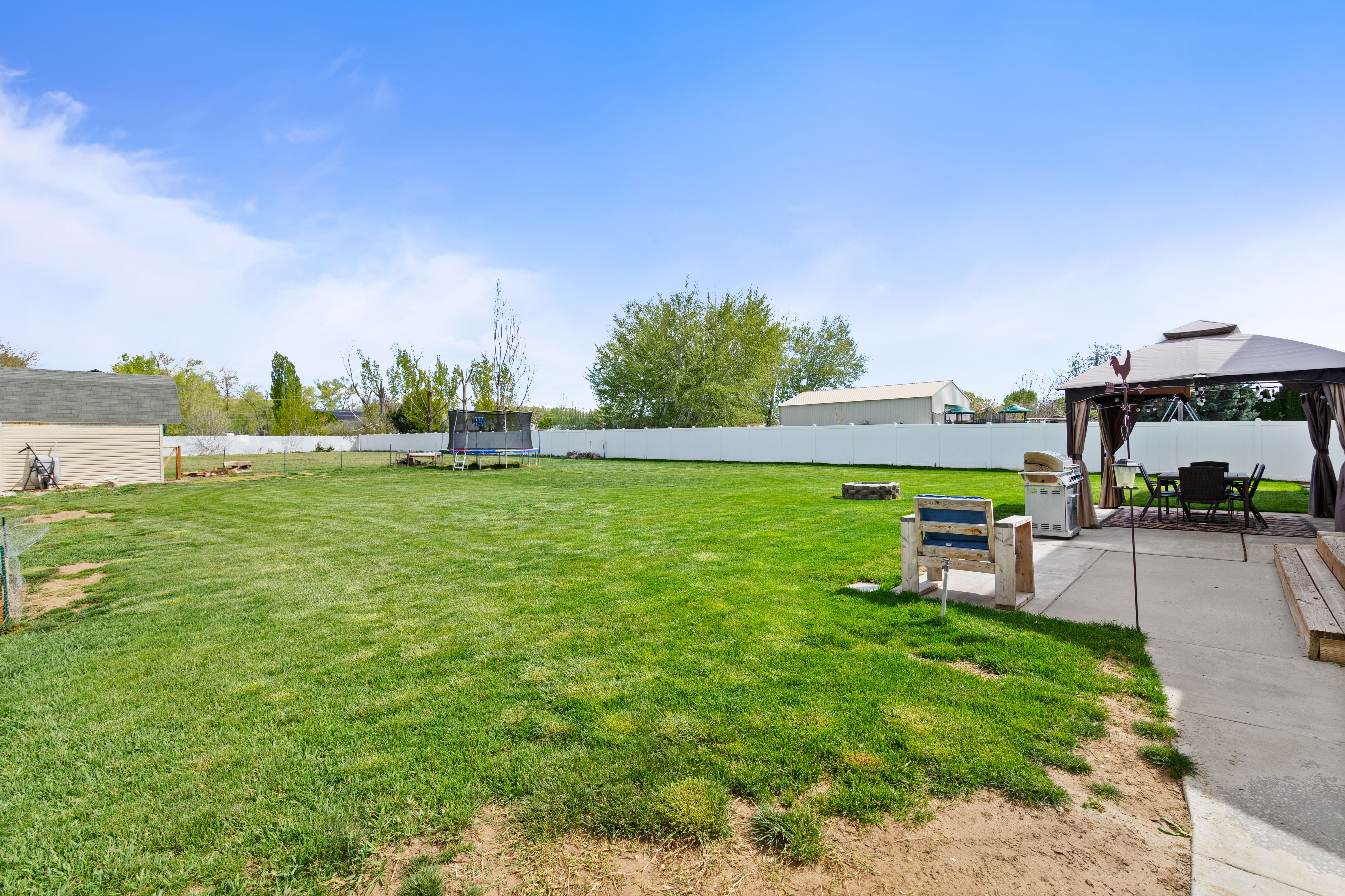 Expansive backyard featuring a lush lawn, white privacy fencing, a dedicated concrete patio, and a storage shed