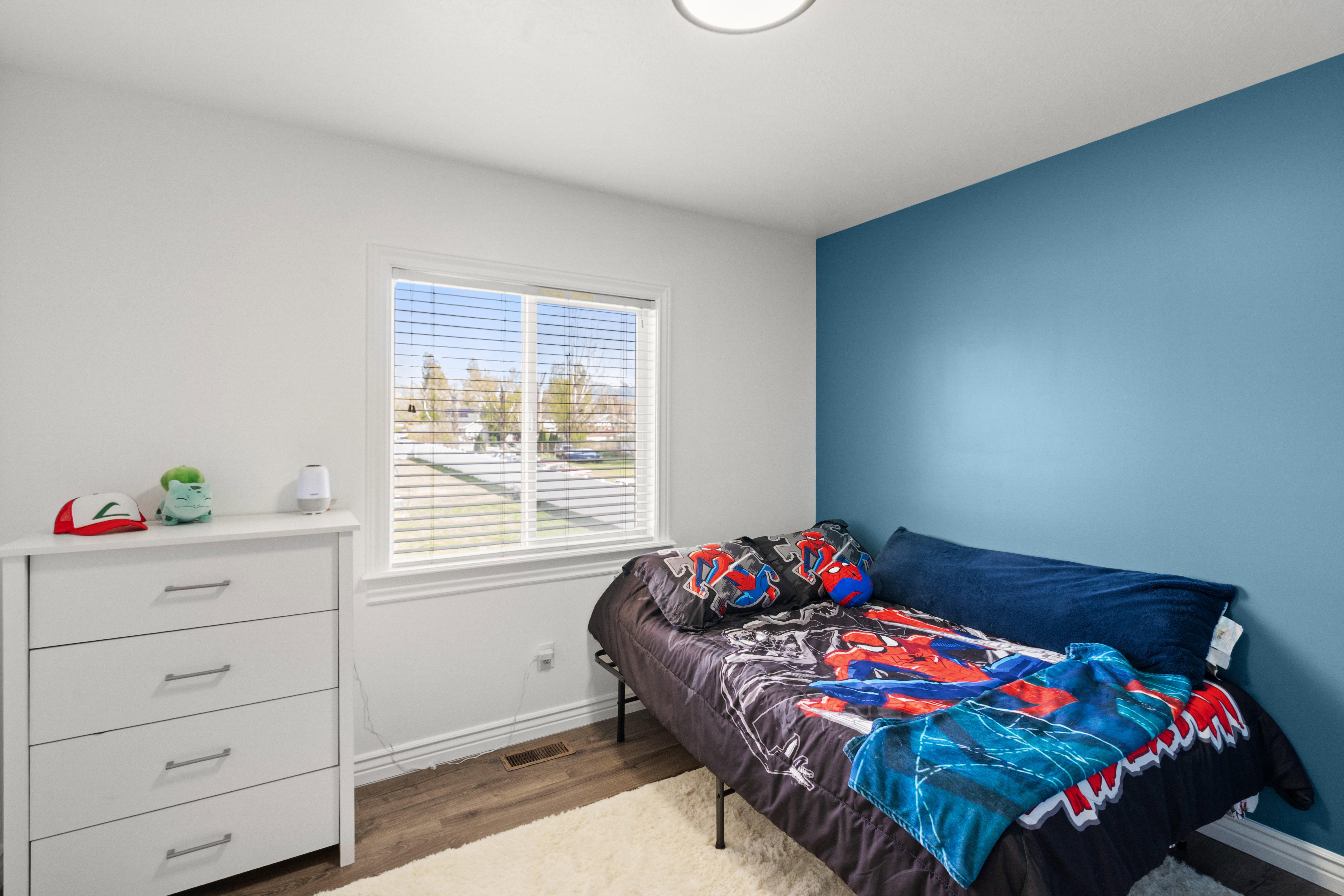 Bedroom featuring a window with white trim, wood-finish flooring, and a blue accent wall