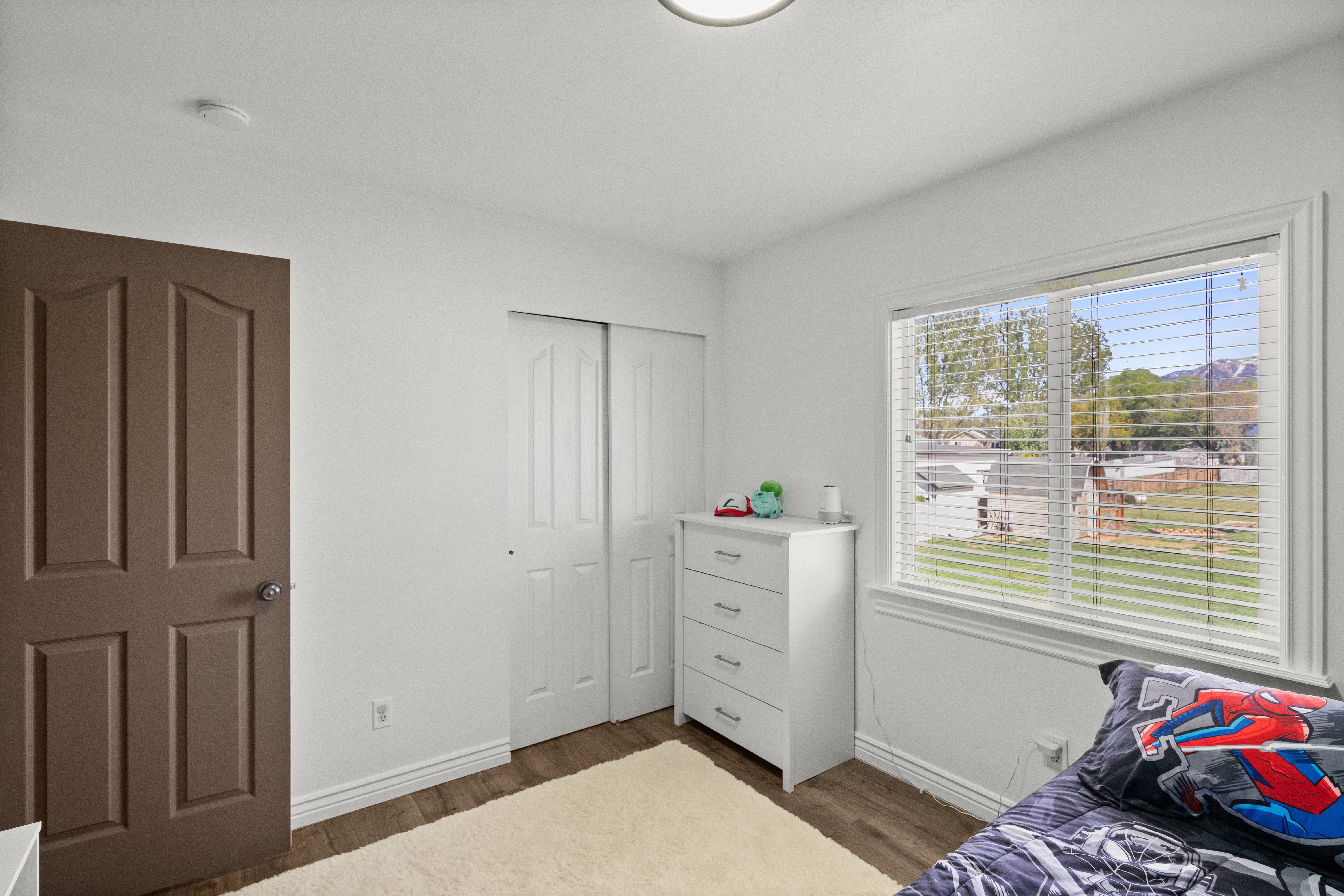 Bedroom featuring wood-finish flooring, white walls, and a window with blinds