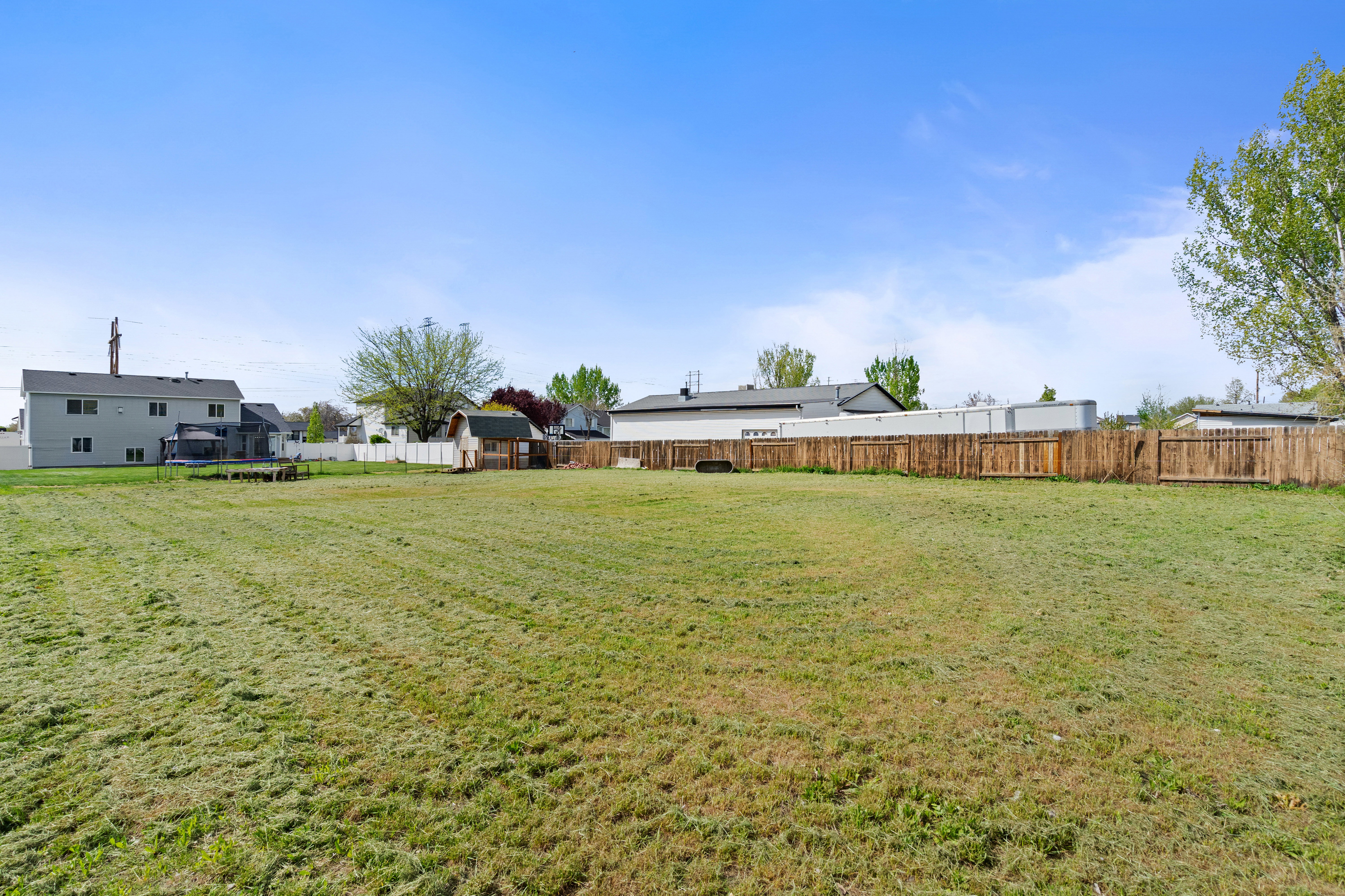 Expansive backyard featuring a large grassy area, a wooden privacy fence, and a small built-in shed