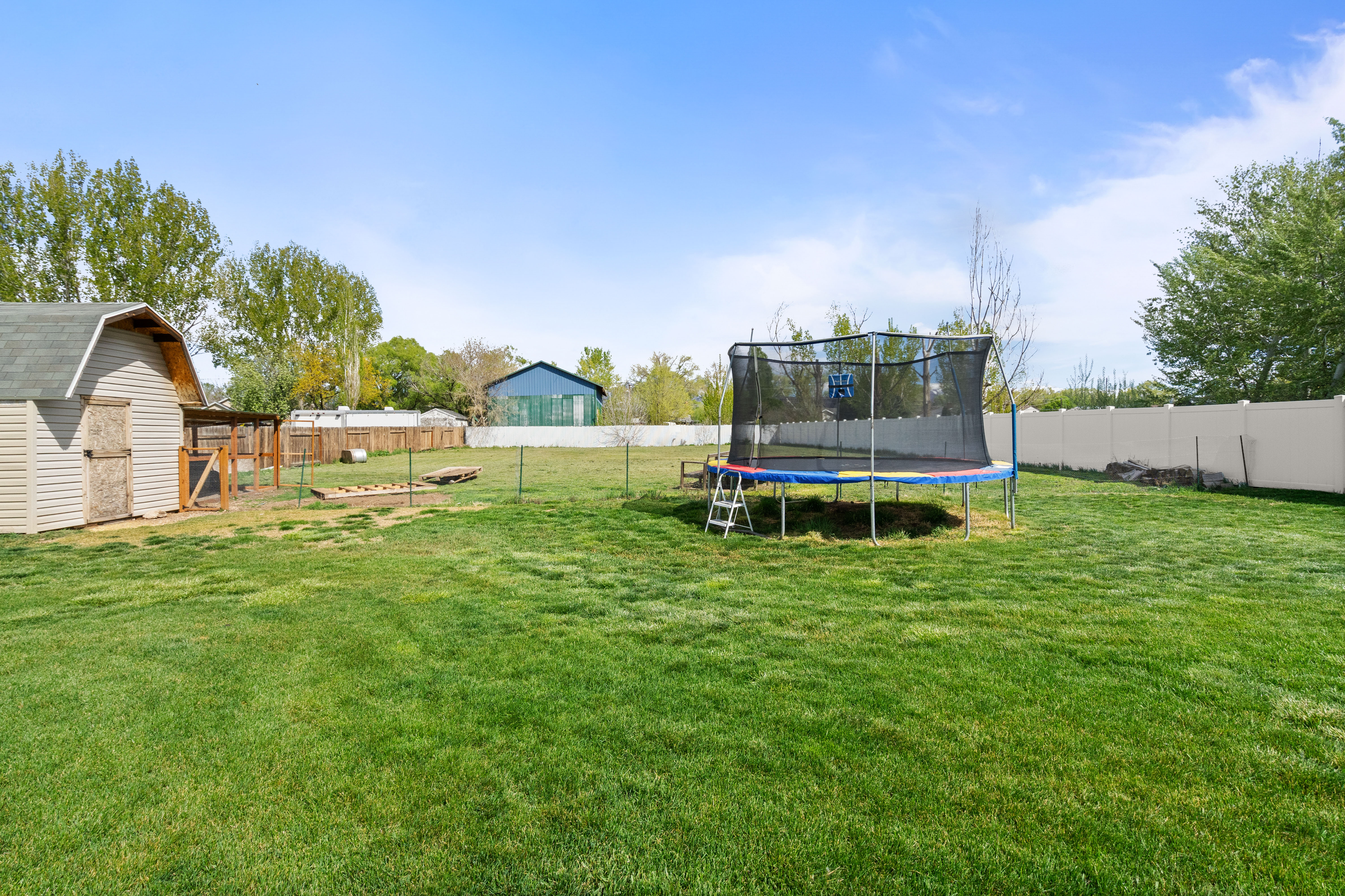 Expansive grassy yard featuring a vinyl privacy fence, a detached shed with light-colored siding and a dark shingle roof, and a wood-framed structure