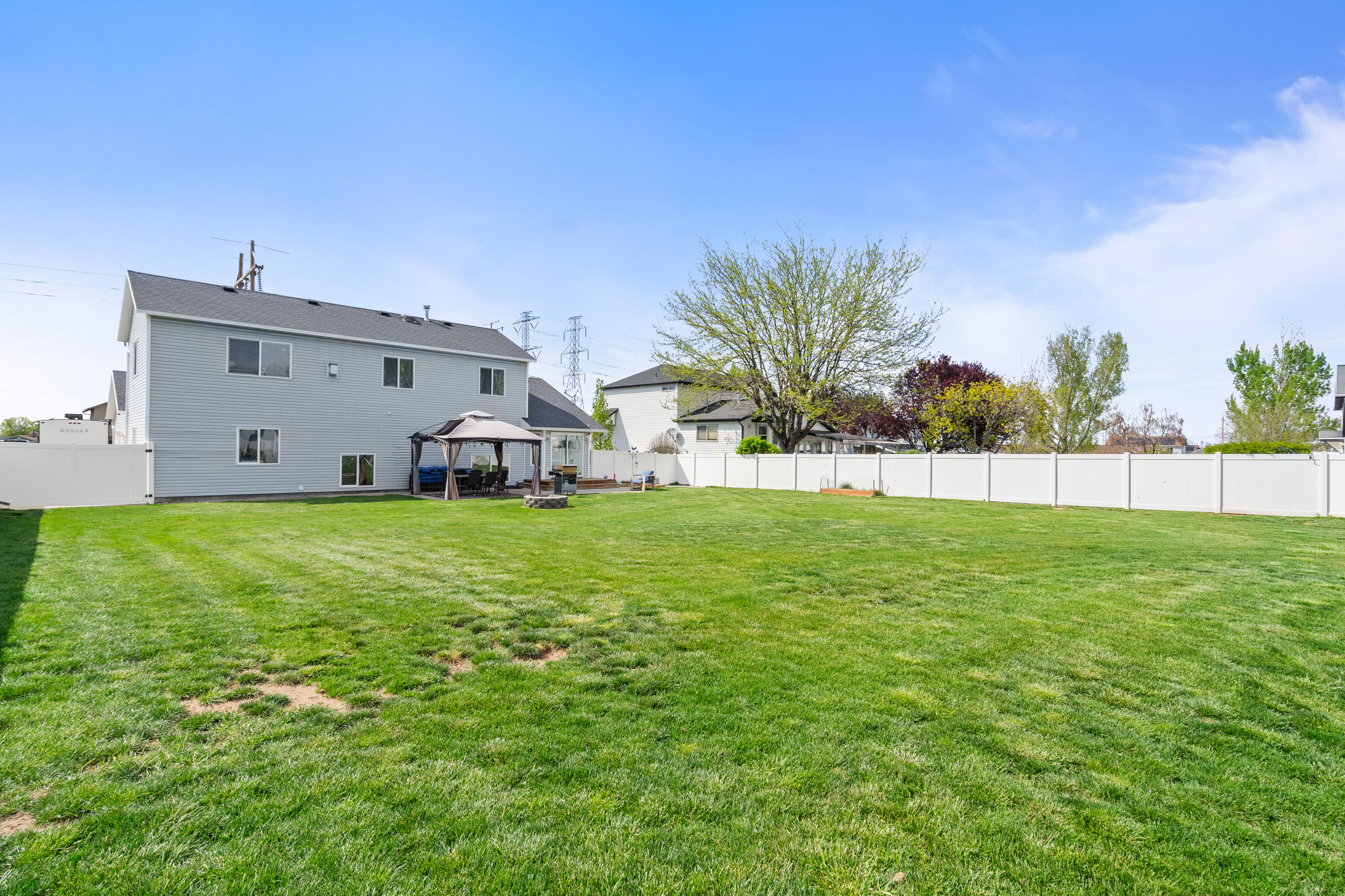 Expansive fenced backyard featuring a large green lawn, a light blue siding exterior, a dark gray roof, and a covered patio area with a gazebo