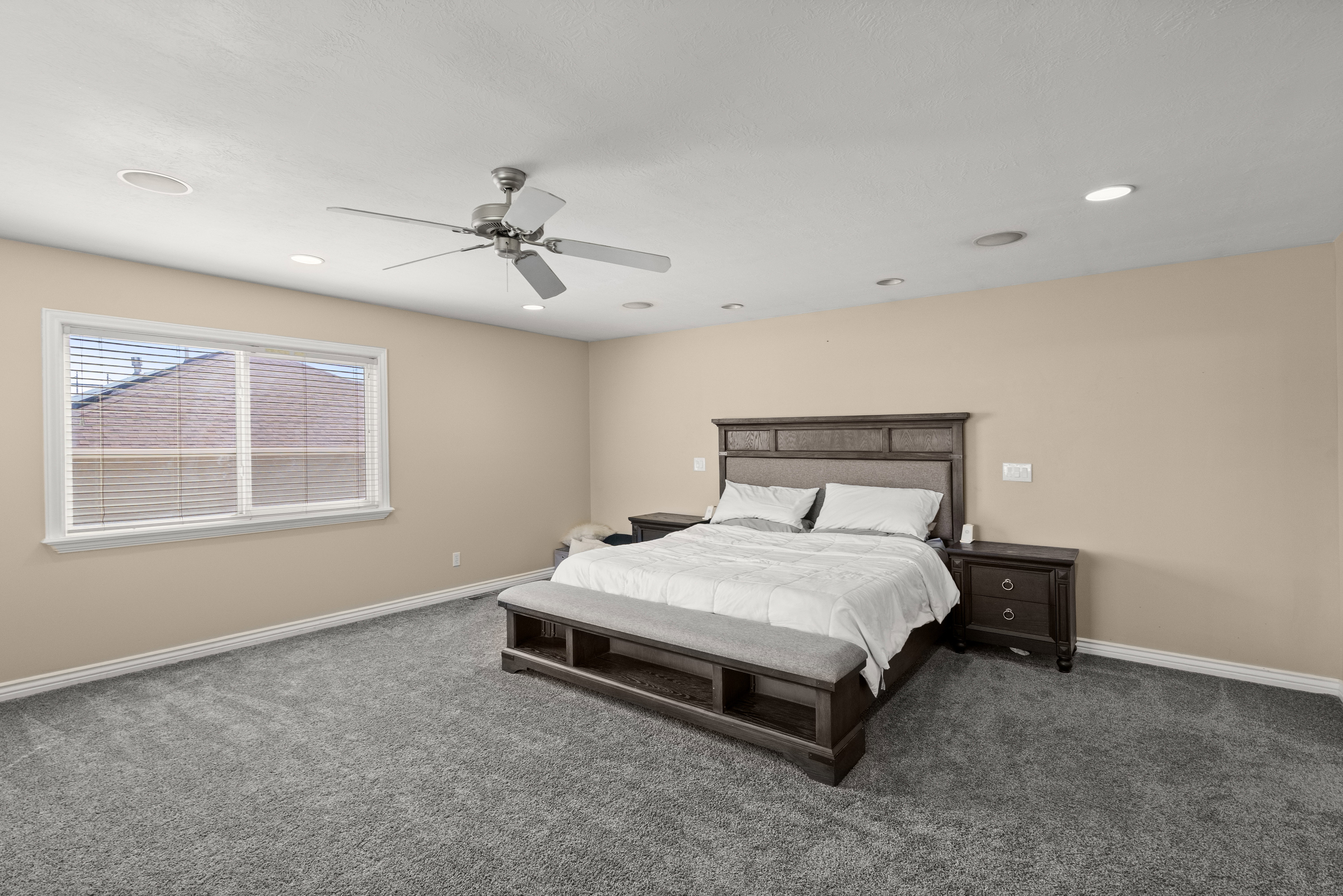 Spacious room featuring neutral wall tones, gray carpeting, a window with horizontal blinds, and recessed lighting