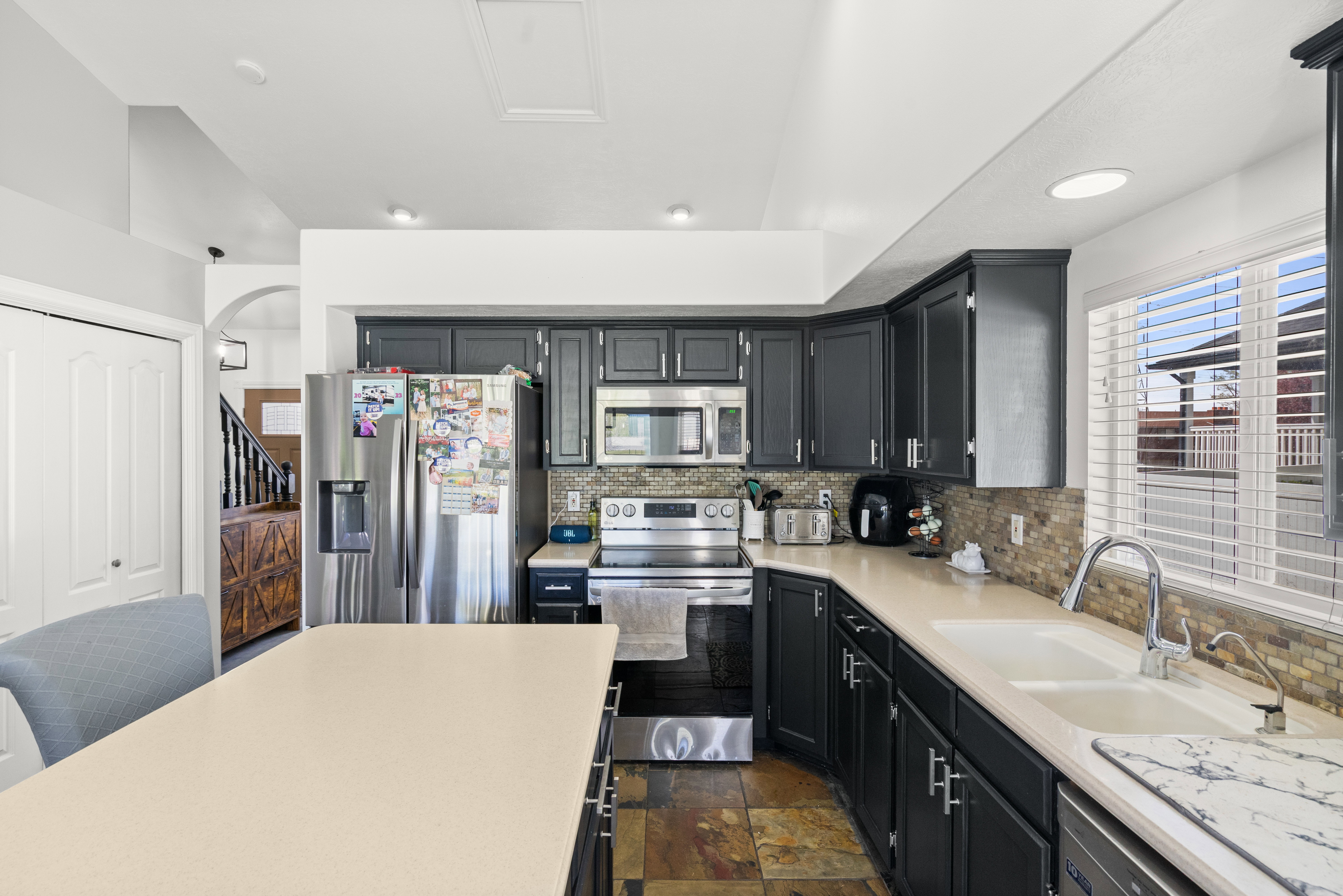 Kitchen featuring dark cabinetry, stainless steel appliances, a light-toned countertop, a tile backsplash, and wood-finish flooring
