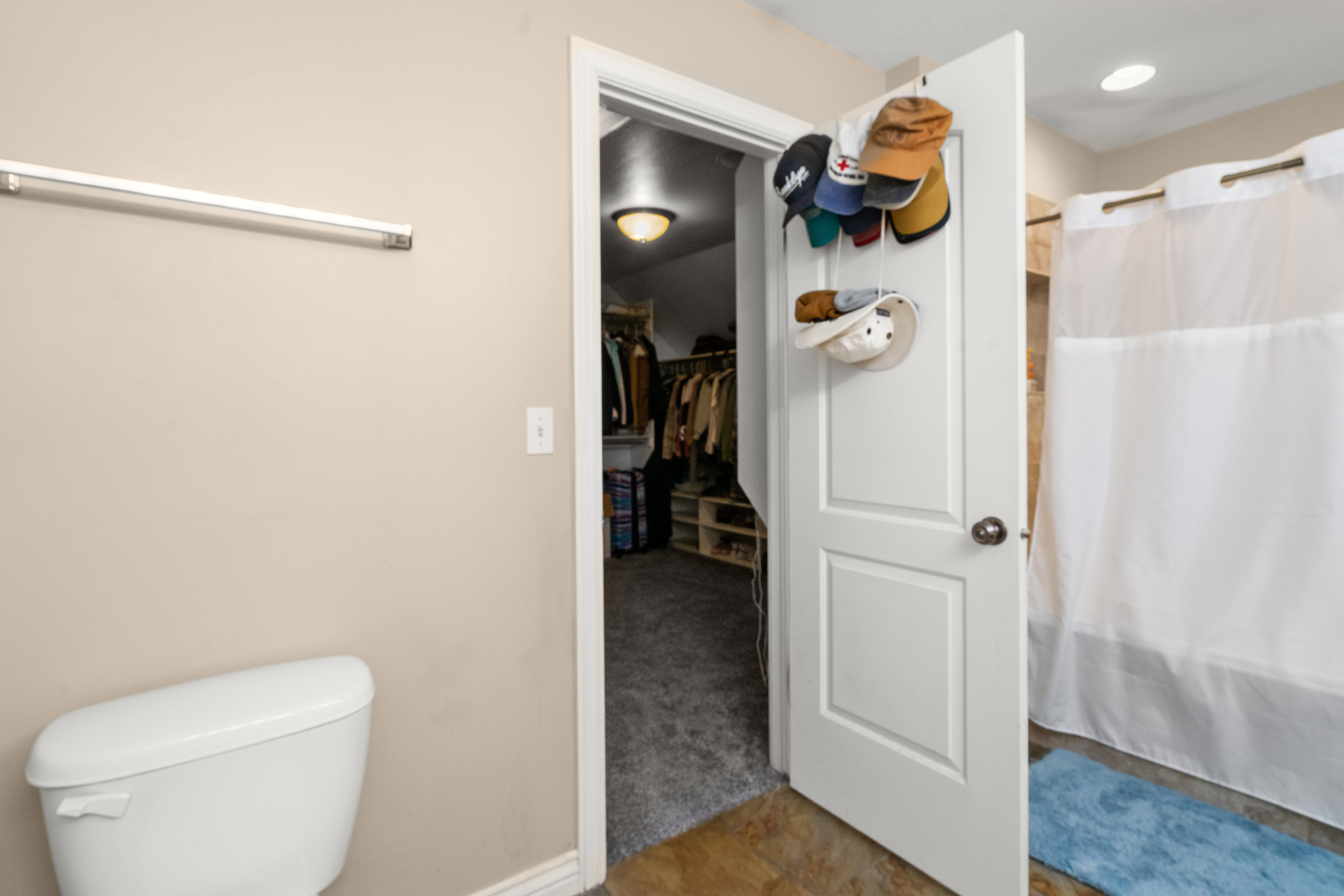 Bathroom featuring a white toilet, light beige wall, and a shower with a white curtain