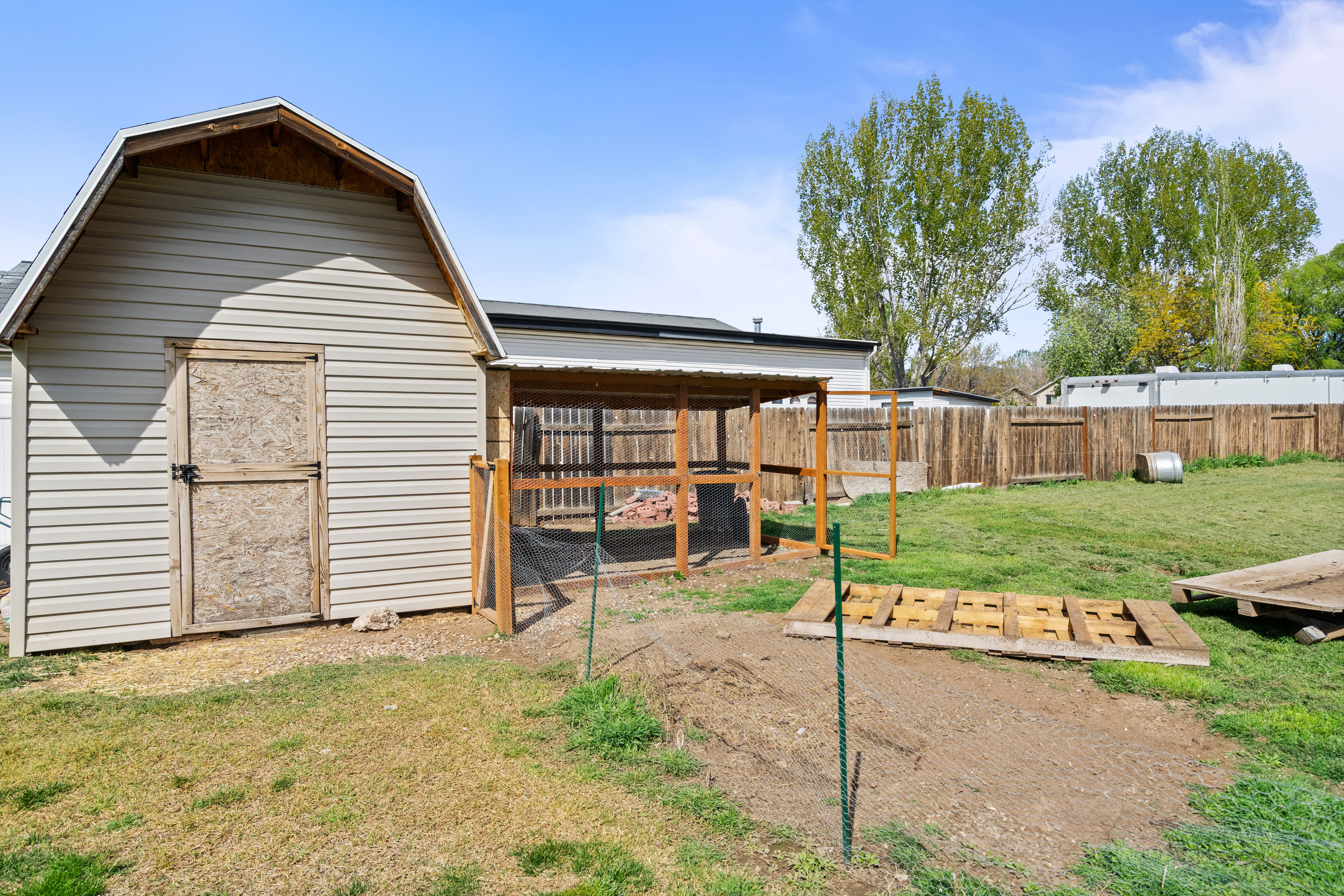 Backyard featuring a light-colored vinyl-sided shed with a gambrel roof and a wooden door