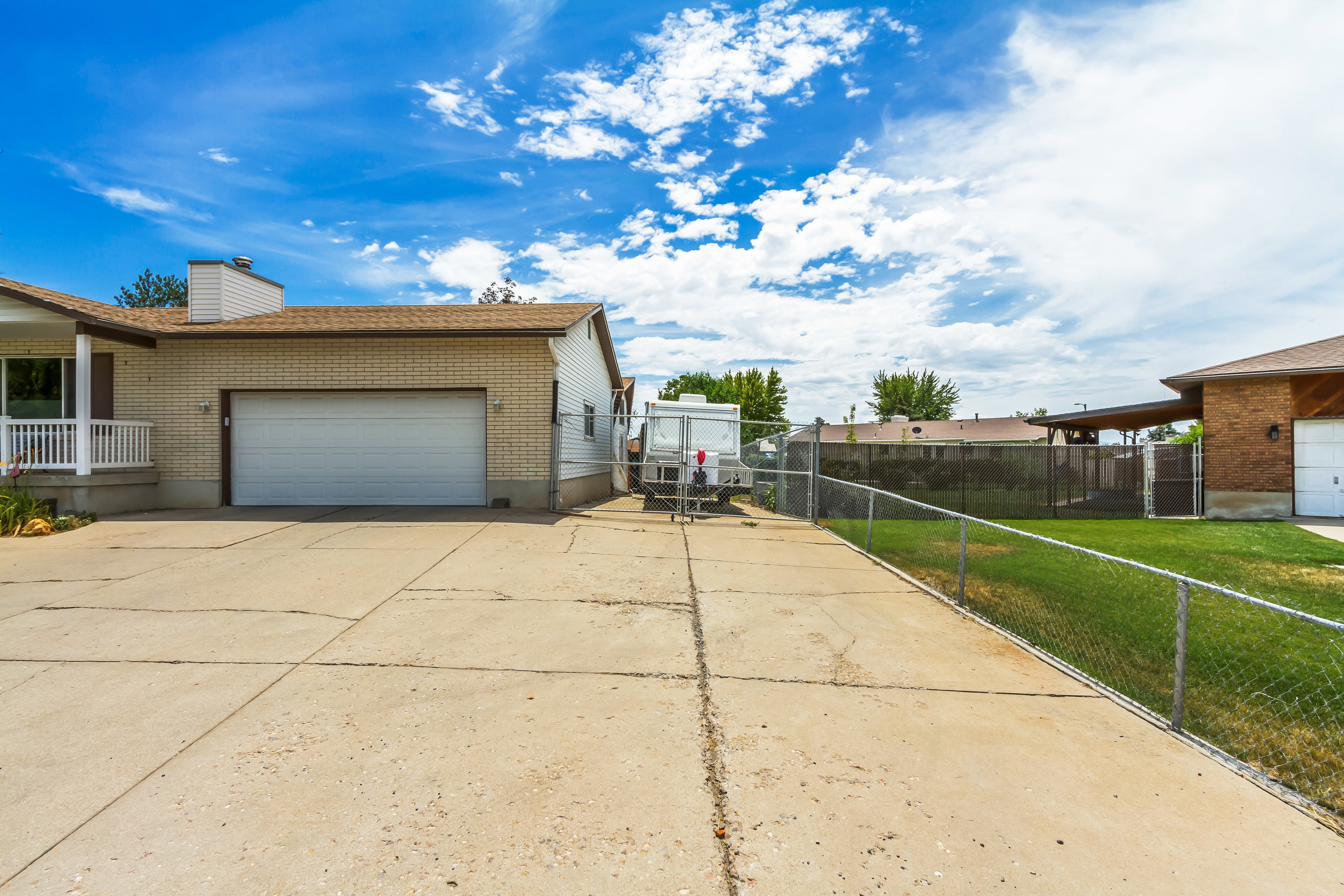 Concrete driveway with a two-car garage, partial brick exterior, and a side access gate
