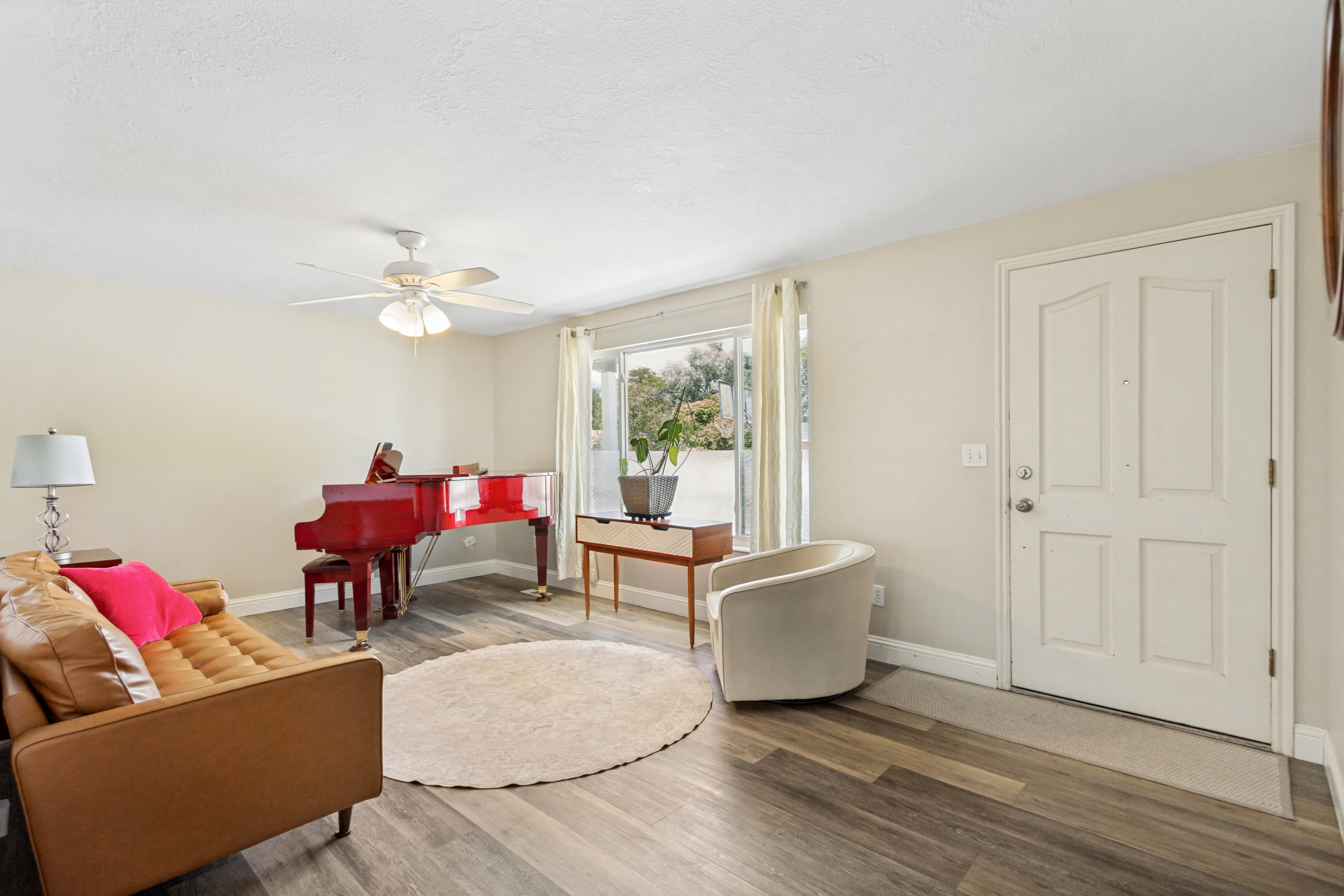 Living area featuring wood-finish flooring, a ceiling fan with integrated lighting, and a paneled entry door