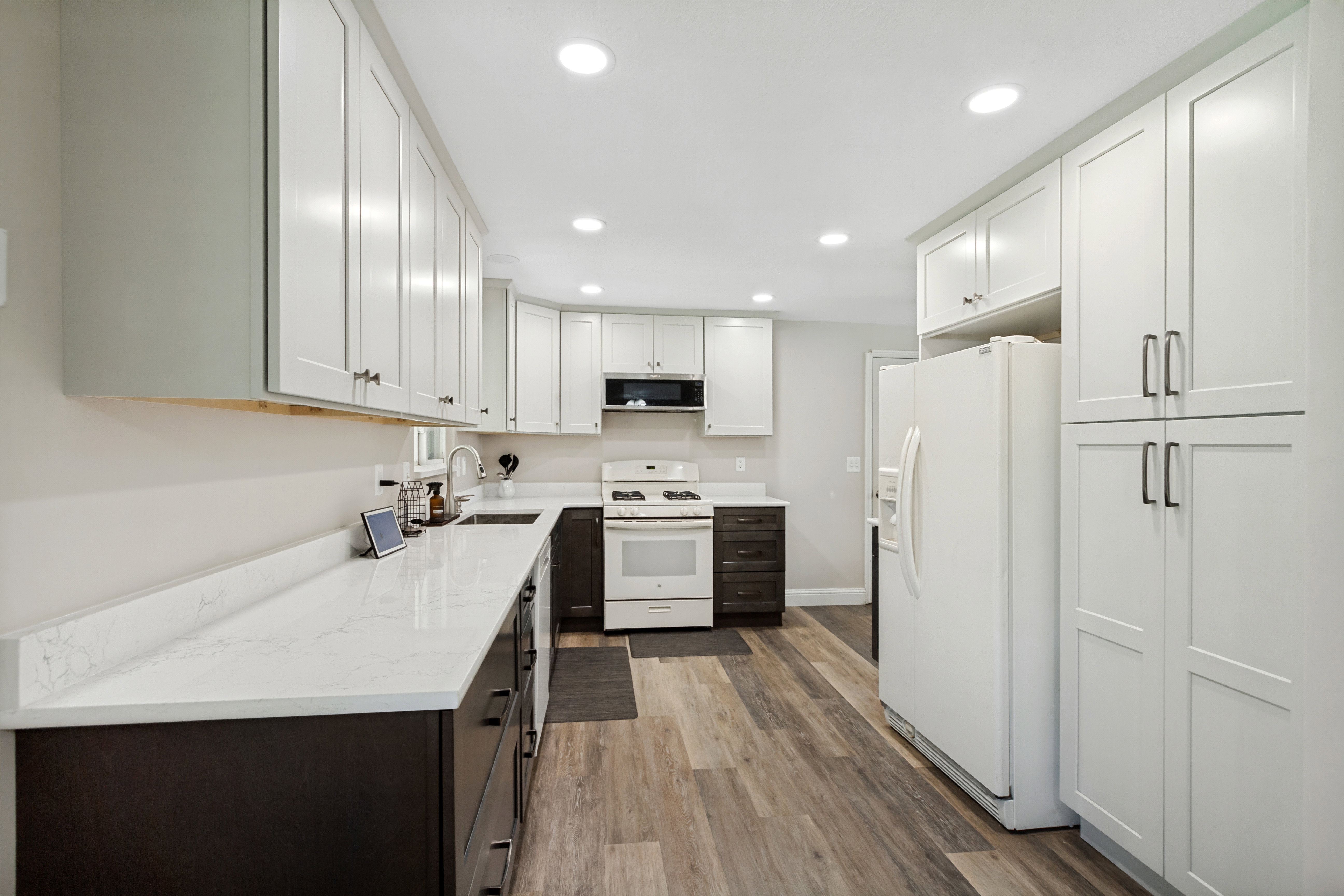 Contemporary kitchen featuring white shaker-style cabinetry, wood-finish flooring, recessed lighting, and white countertops