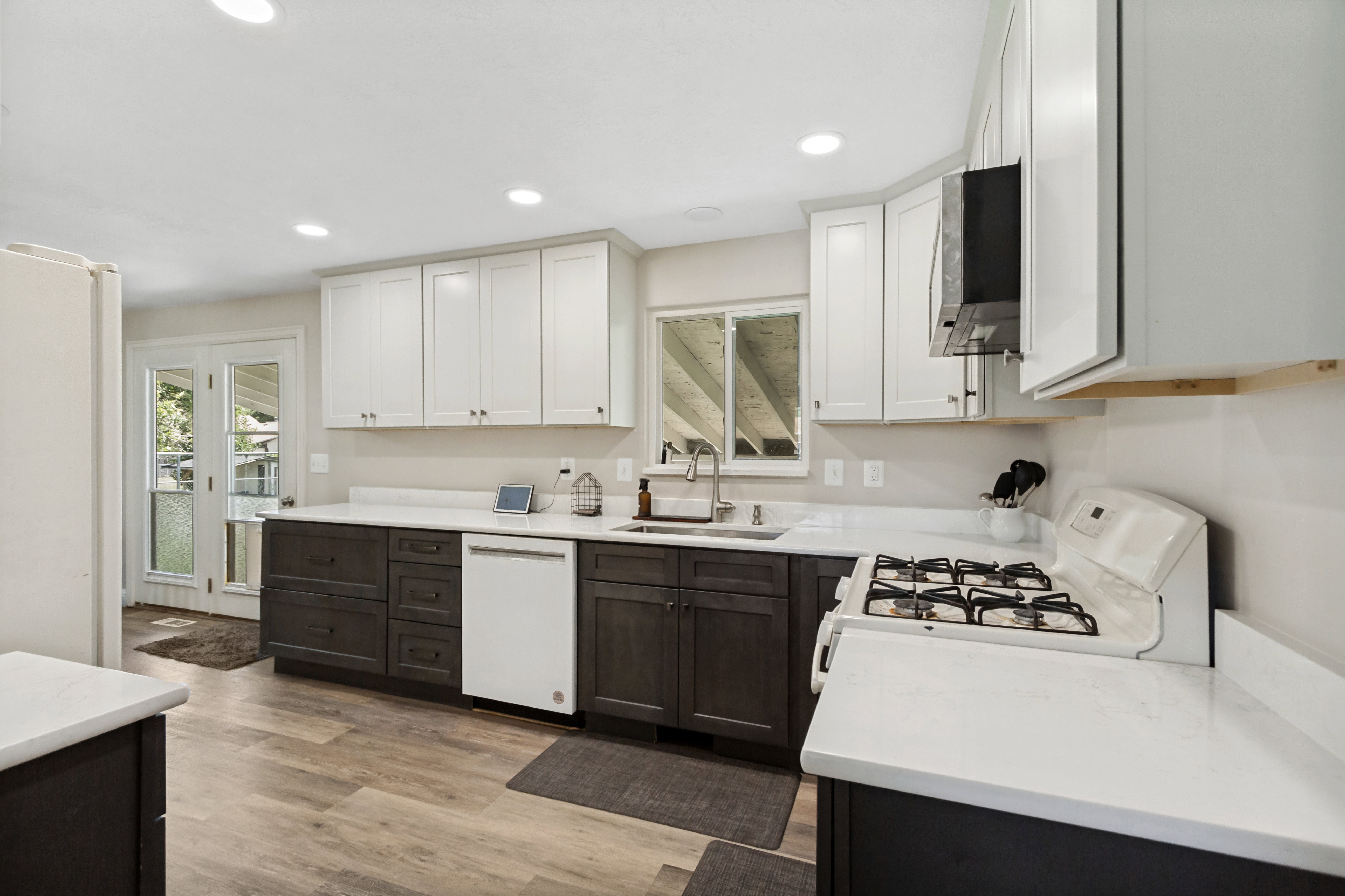 Kitchen featuring two-tone cabinetry with upper white cabinets and lower dark wood-finish cabinets, a gas range, white countertops, and wood-finish flooring