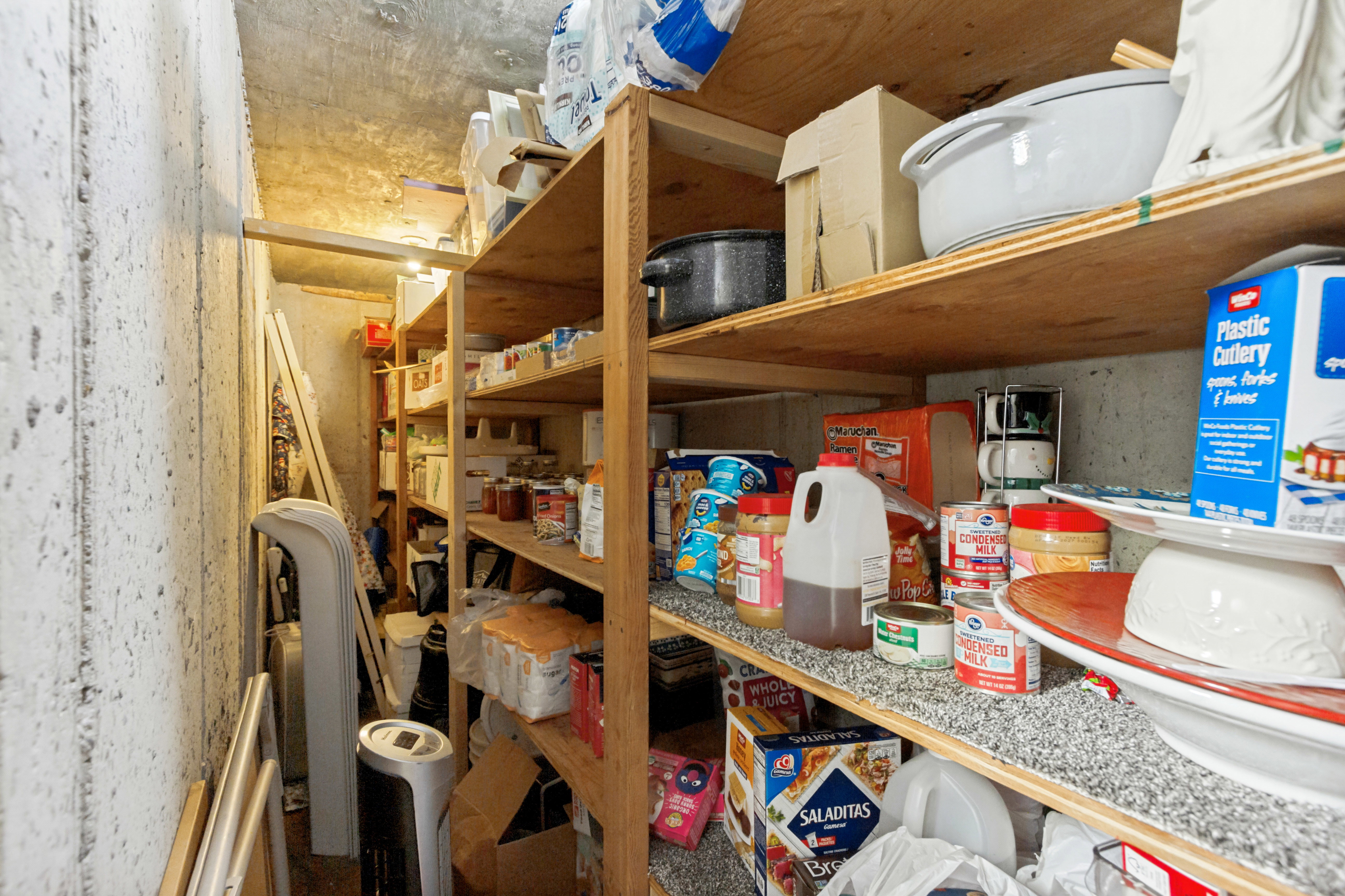 Storage area with concrete walls and ceiling, featuring built-in wooden shelving for organization