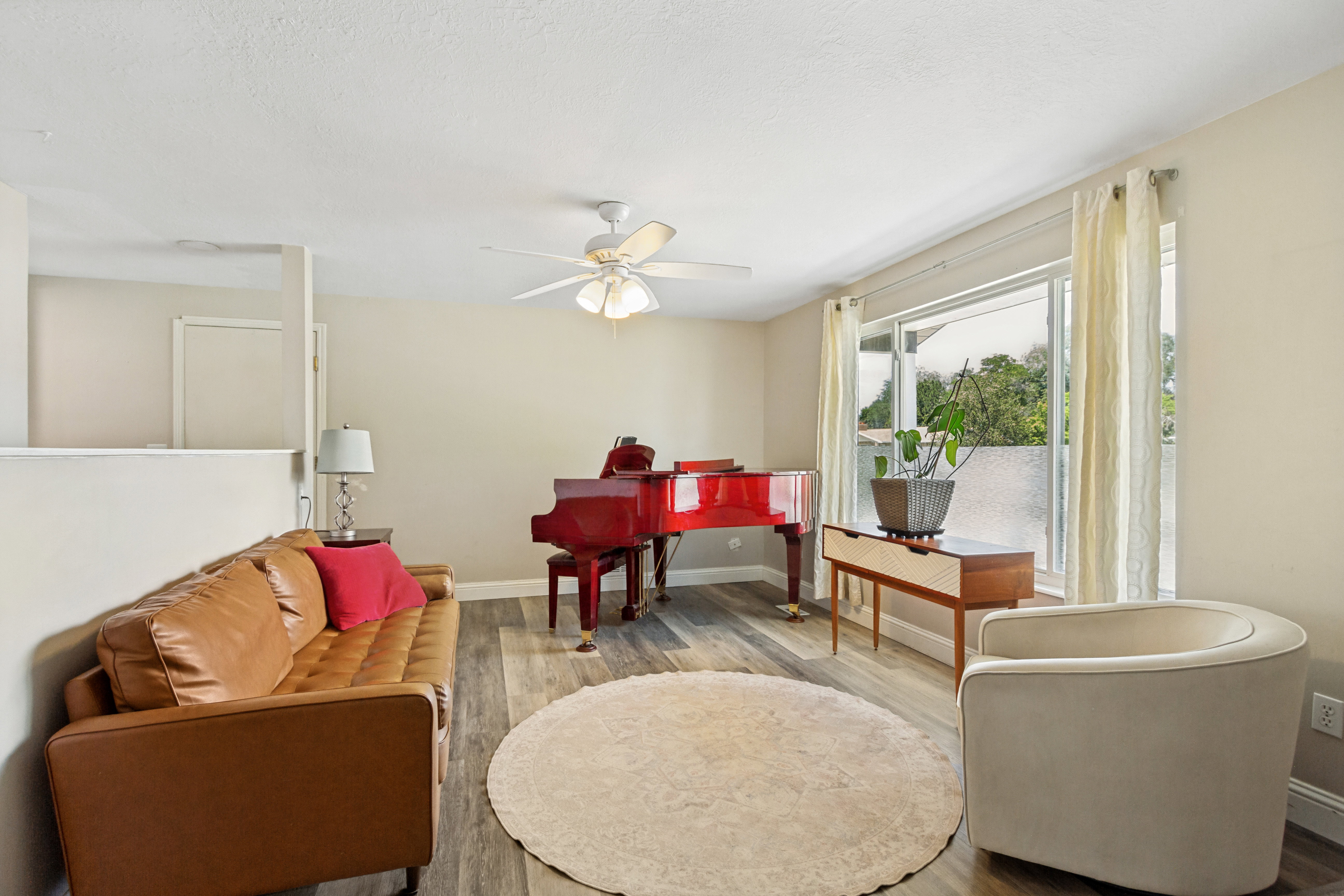 Living area featuring wood-finish flooring, a ceiling fan with integrated lighting, and a large window with vertical blinds
