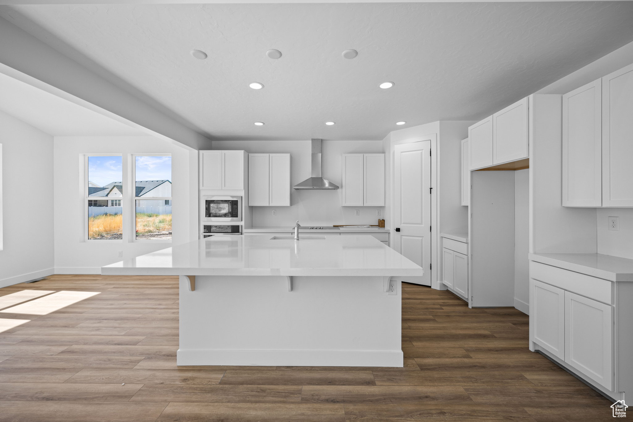 Open-concept kitchen featuring an expansive island, white cabinetry, integrated stainless steel appliances, recessed ceiling lights, and wood-finish flooring. This is not the actual home being built but a representation of the features available in this h