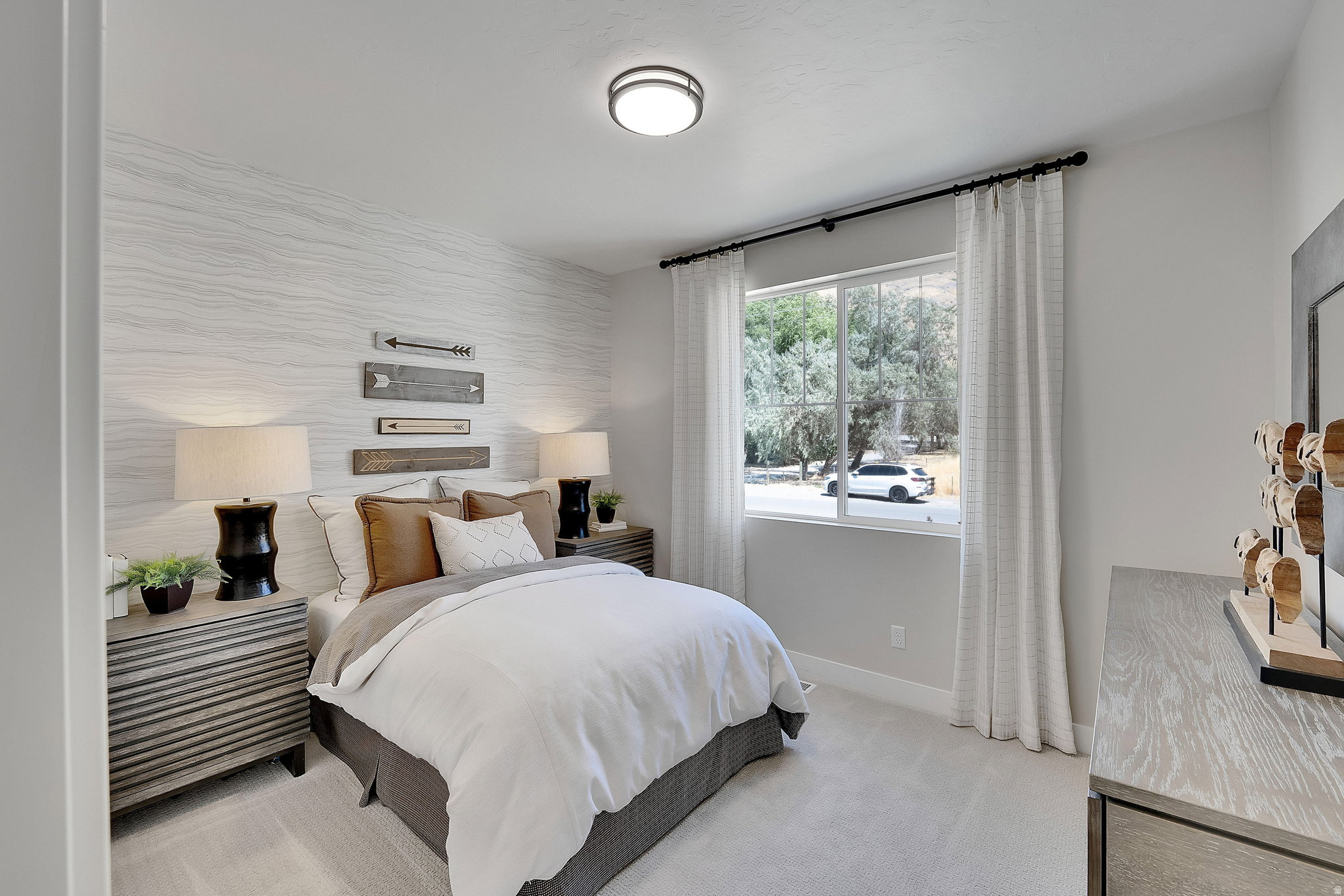 Bedroom featuring a textured accent wall, light-toned carpeting, and a large window with white curtain panels. This is not the actual home being built but a representation of the features available in this home. Colors and finishes may differ from those s