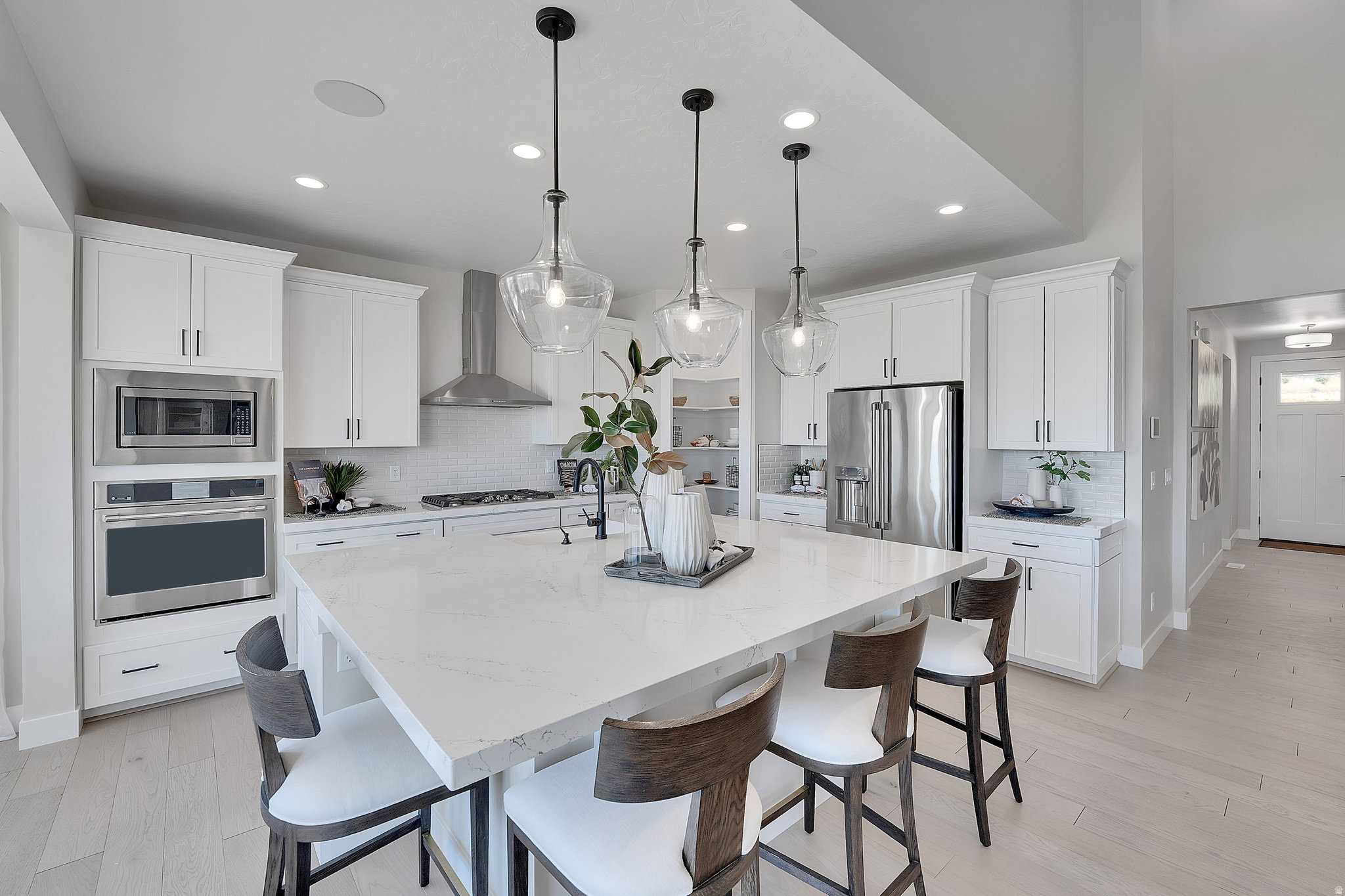 Bright kitchen featuring a large central island with seating, white shaker cabinetry, stainless steel appliances, and wood-finish flooring. This is not the actual home being built but a representation of the features available in this home. Colors and fin