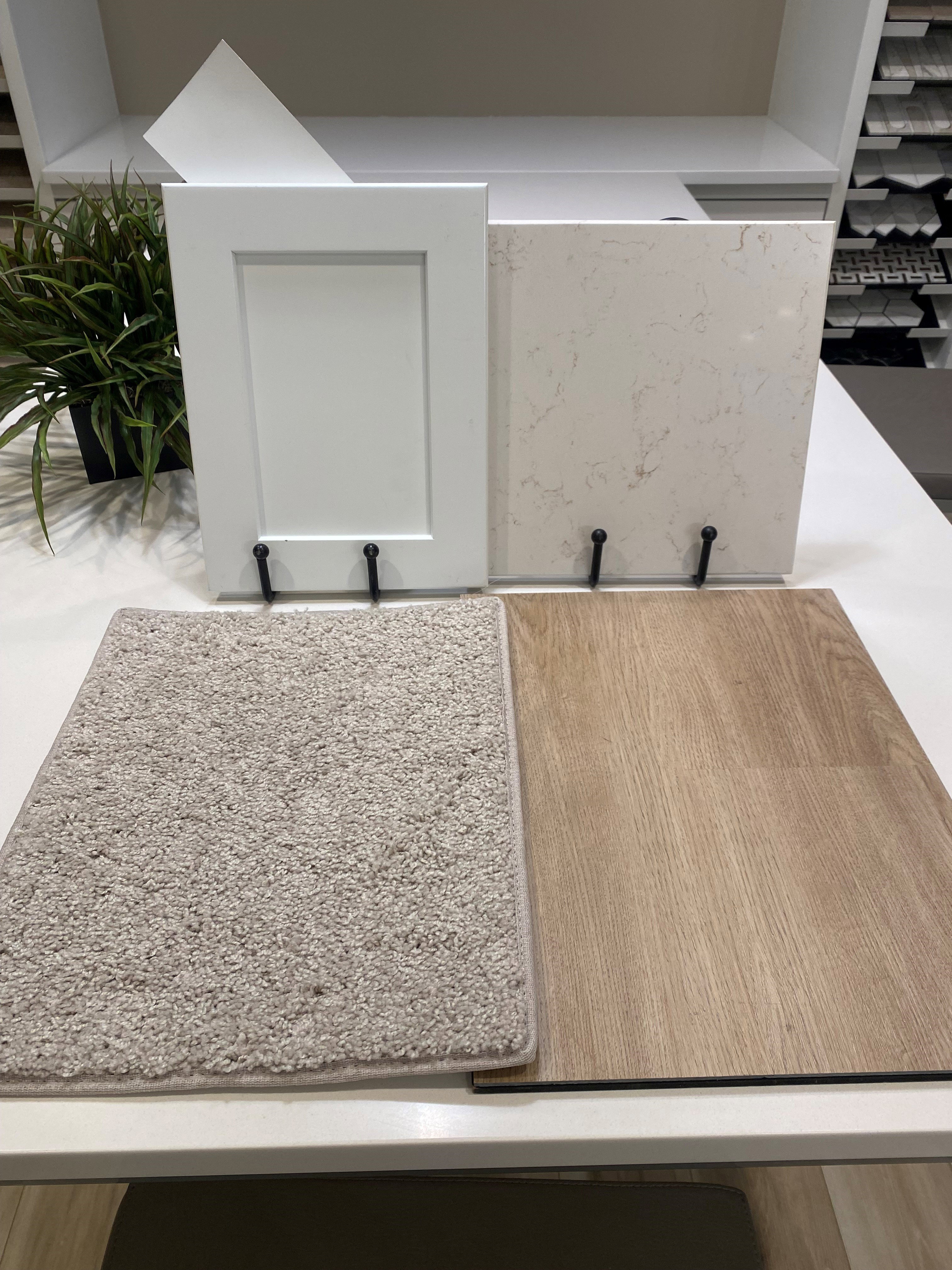 Sample board featuring a white shaker-style cabinet door, a light-toned countertop with subtle veining, light-colored carpet, and wood-finish flooring