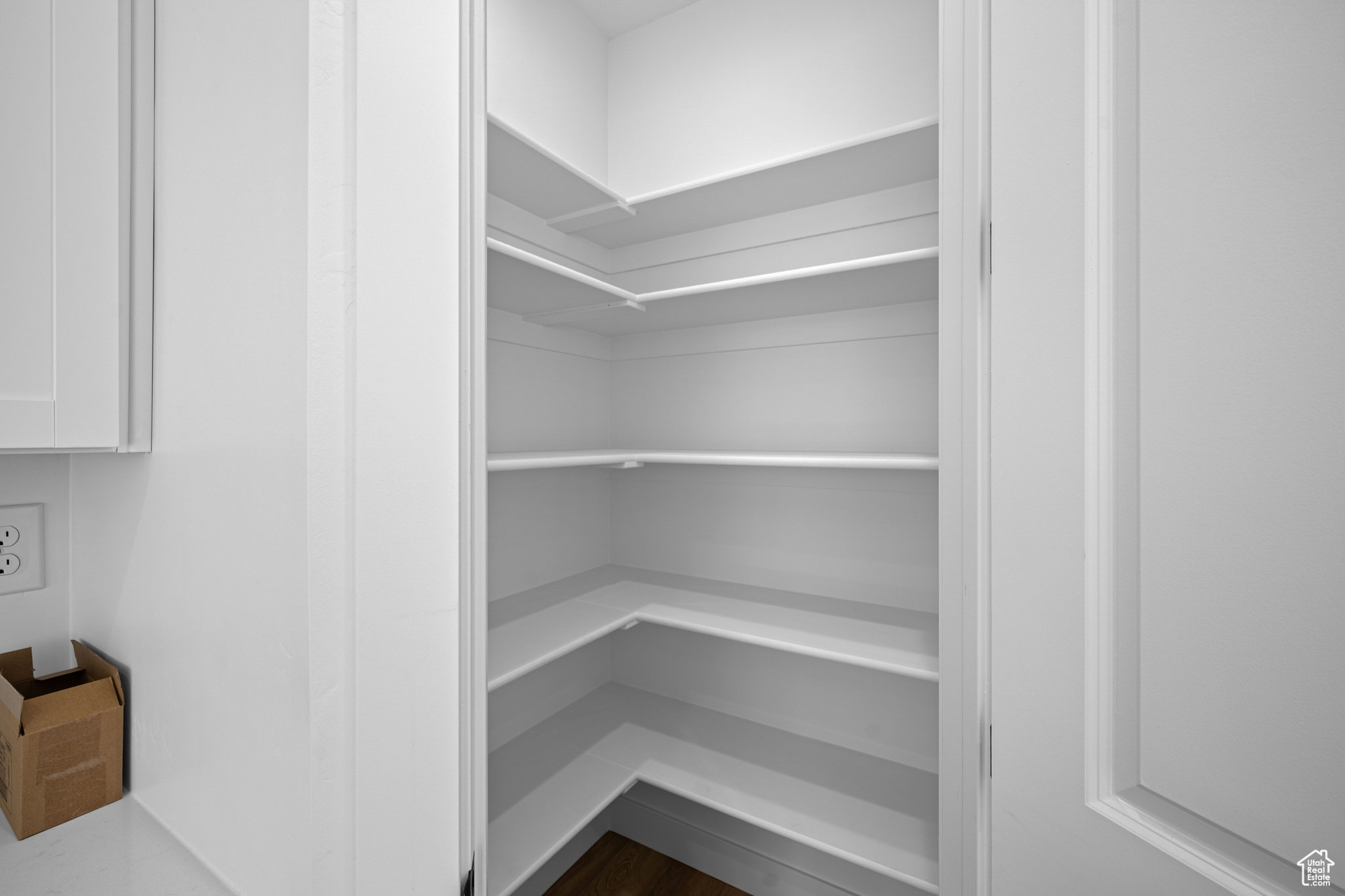 Walk-in pantry featuring multiple levels of white shelving, wood-finish flooring, and white walls. This is not the actual home being built but a representation of the features available in this home. Colors and finishes may differ from those shown.