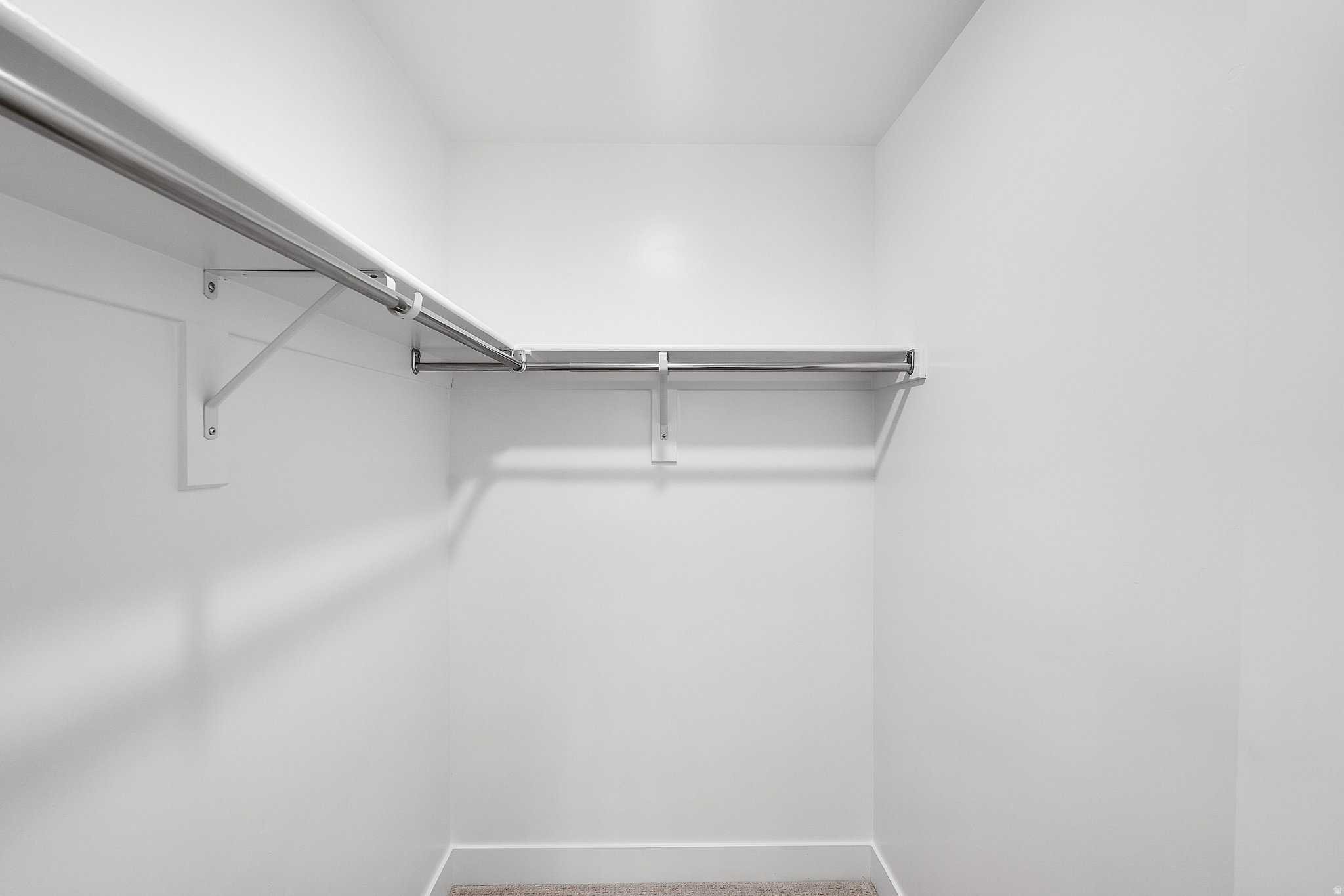 Walk-in closet with white walls, L-shaped shelving, and metal hanging rods. This is not the actual home being built but a representation of the features available in this home. Colors and finishes may differ from those shown.