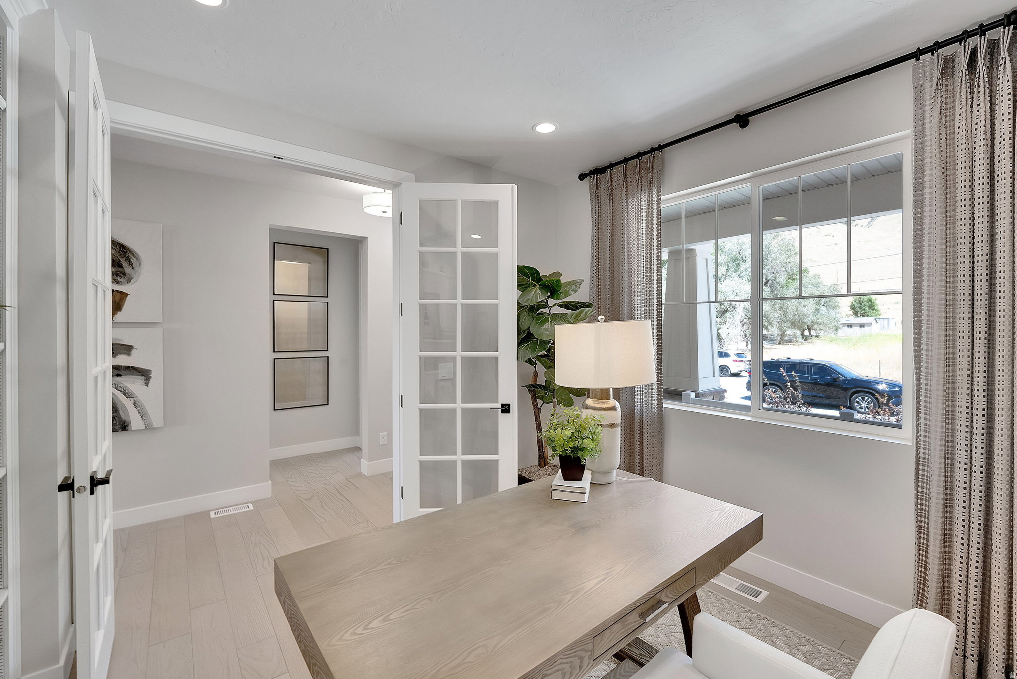 French doors with clear glass panels open to a bright room featuring wood-finish flooring, recessed lighting, and a large multi-pane window. This is not the actual home being built but a representation of the features available in this home. Colors and fi