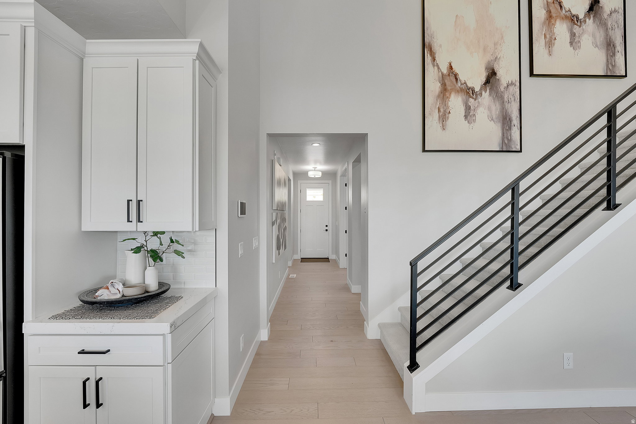 Entryway featuring light wood-finish flooring, a modern black metal staircase railing, and a white paneled door. This is not the actual home being built but a representation of the features available in this home. Colors and finishes may differ from those