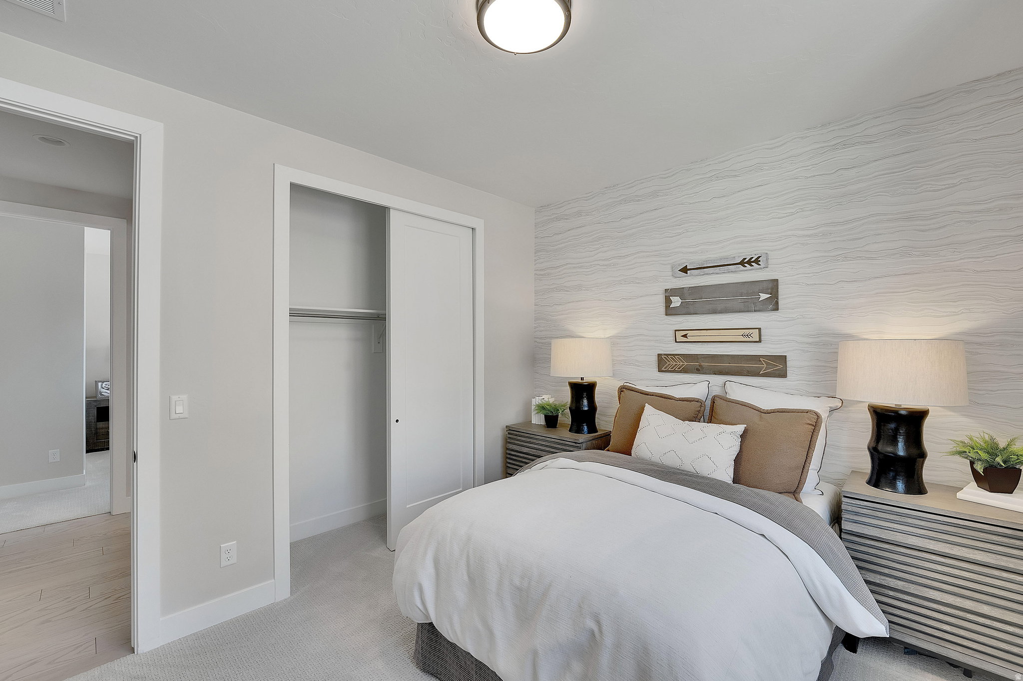 Bedroom featuring a patterned accent wall, light gray carpeting, and a built-in closet with sliding doors. This is not the actual home being built but a representation of the features available in this home. Colors and finishes may differ from those shown