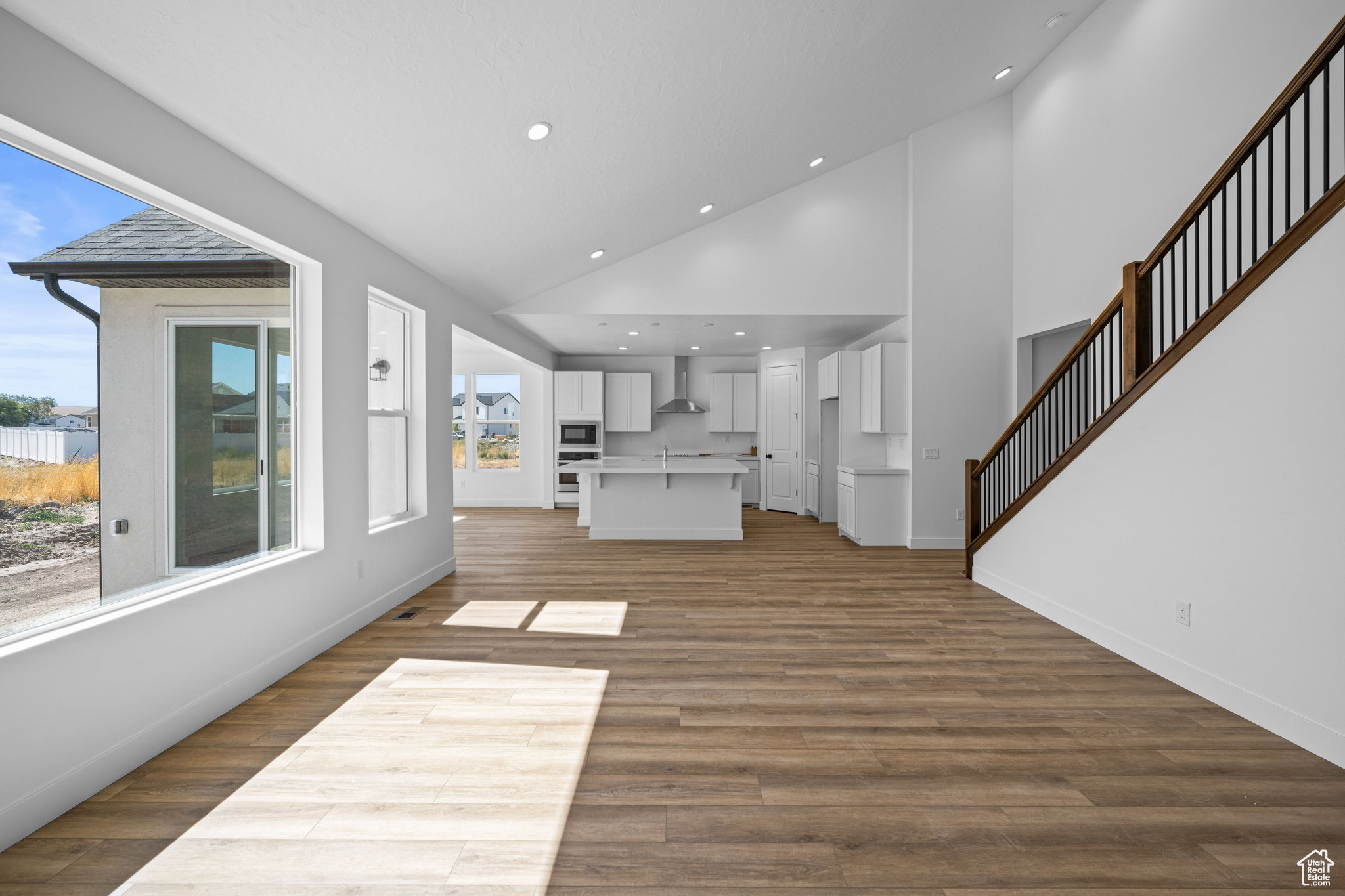 Open-concept main living area featuring wood-finish flooring, high vaulted ceilings with recessed lighting, and a contemporary staircase. This is not the actual home being built but a representation of the features available in this home. Colors and finis