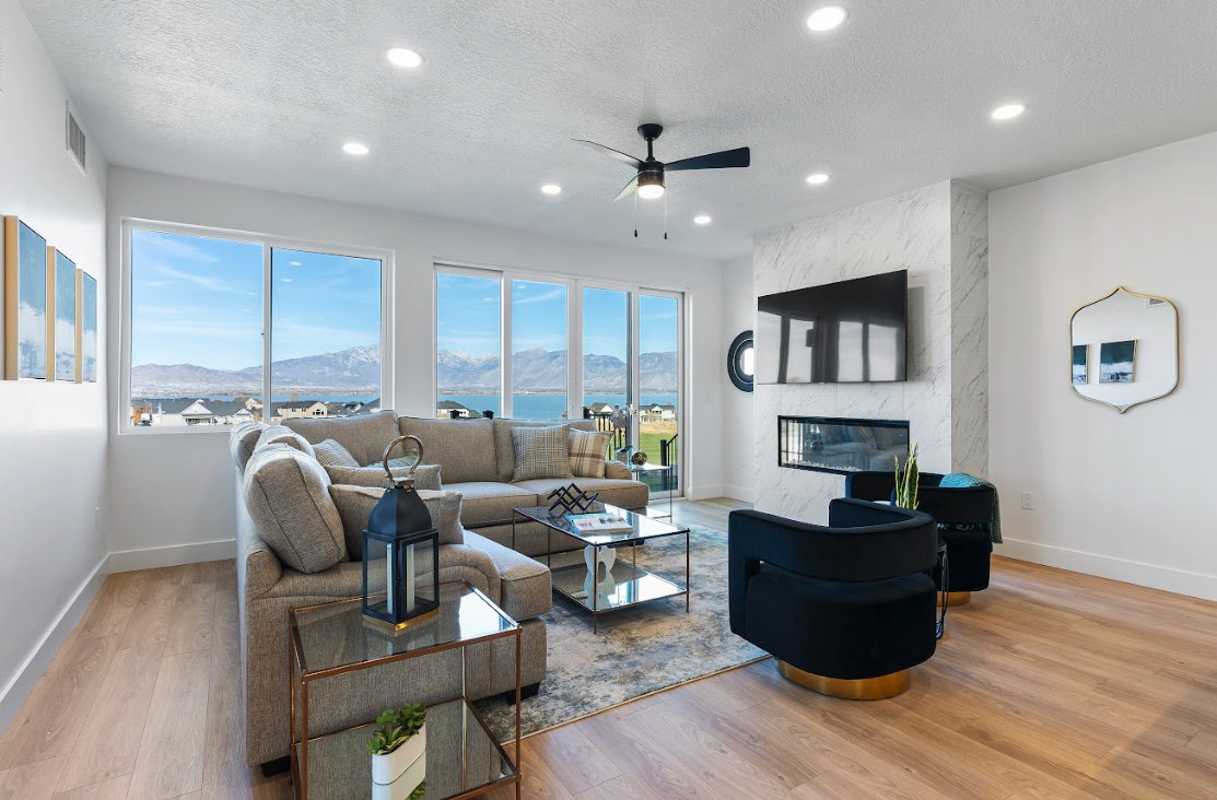 Living area featuring expansive windows, wood-finish flooring, a contemporary fireplace with a stone-finish surround, recessed lighting, and a ceiling fan