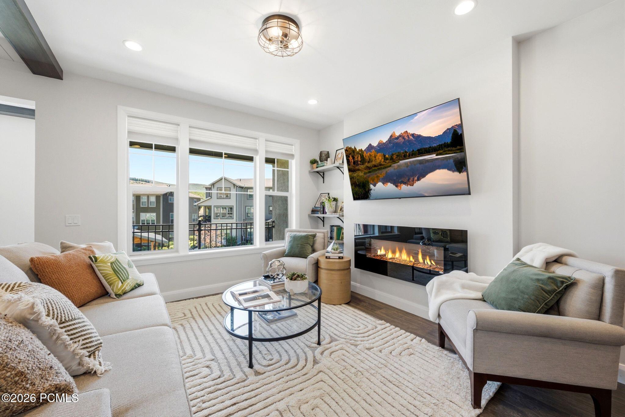 Living space featuring a linear electric fireplace, wood-finish flooring, recessed lighting, and a multi-pane window with a balcony