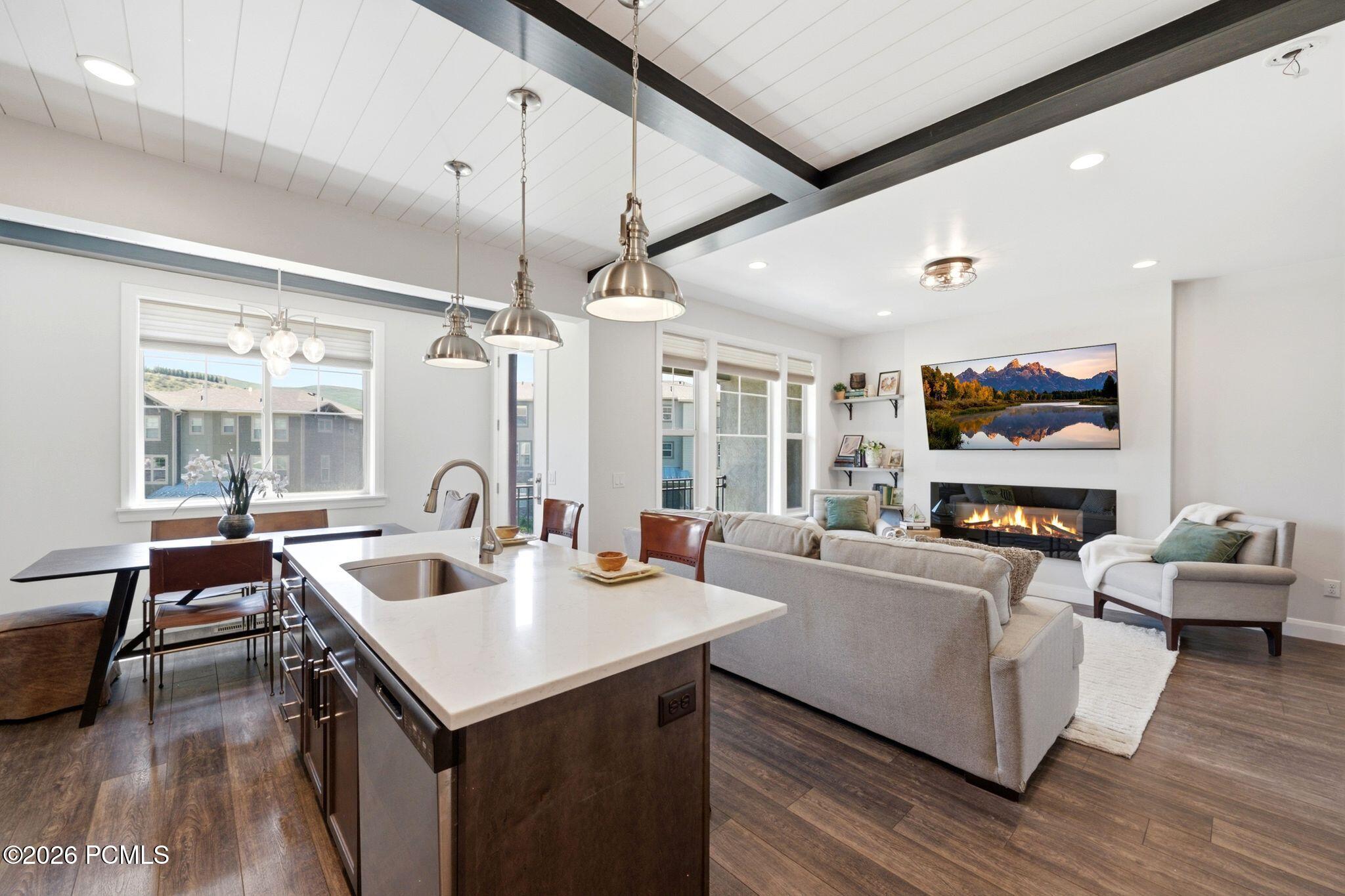 Open-concept living area featuring wood-finish flooring, a contemporary linear fireplace, and a kitchen island with a stainless steel sink and white countertop