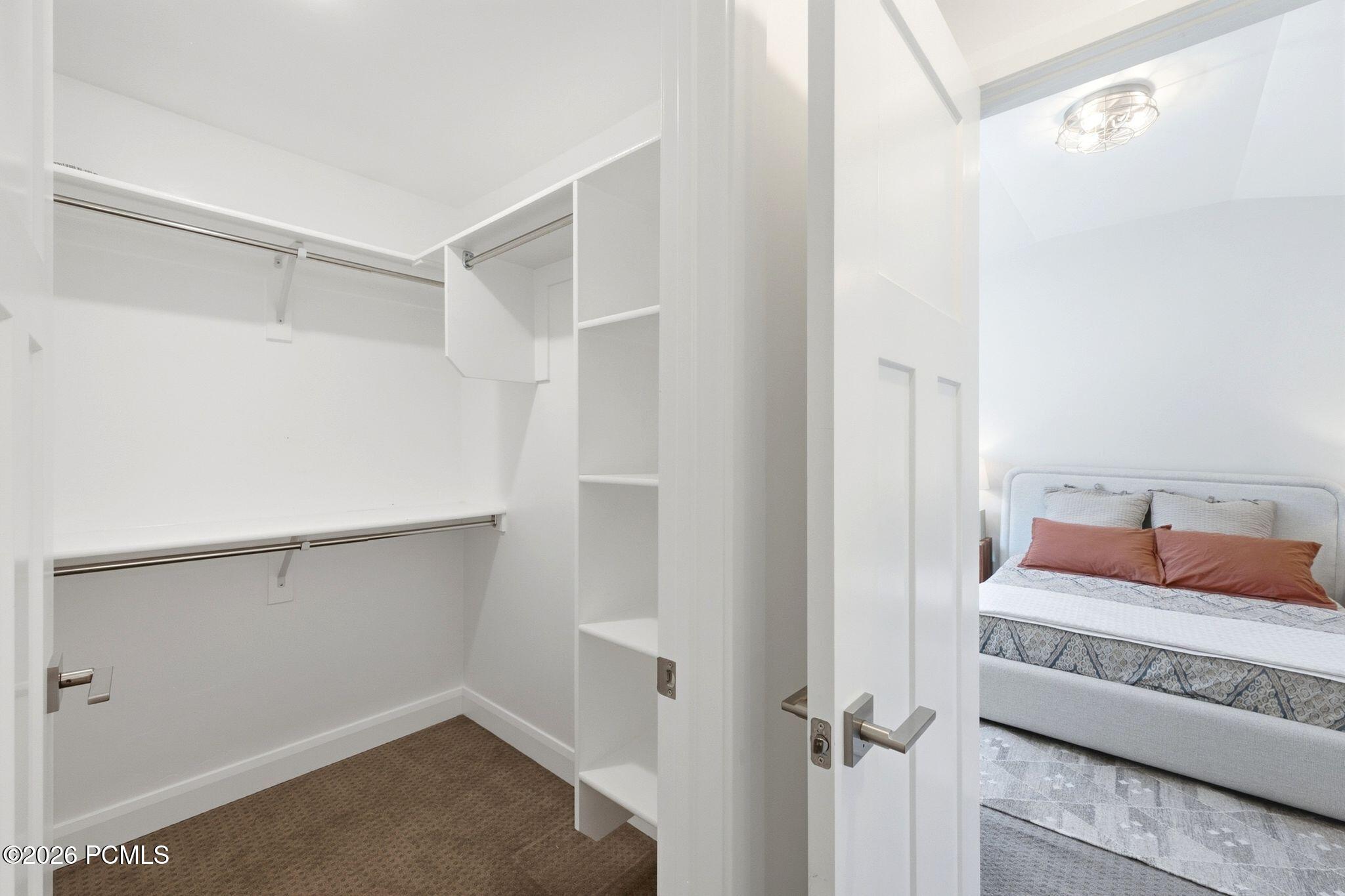 Walk-in closet featuring white built-in shelving, dual hanging rods, and neutral-toned carpeting