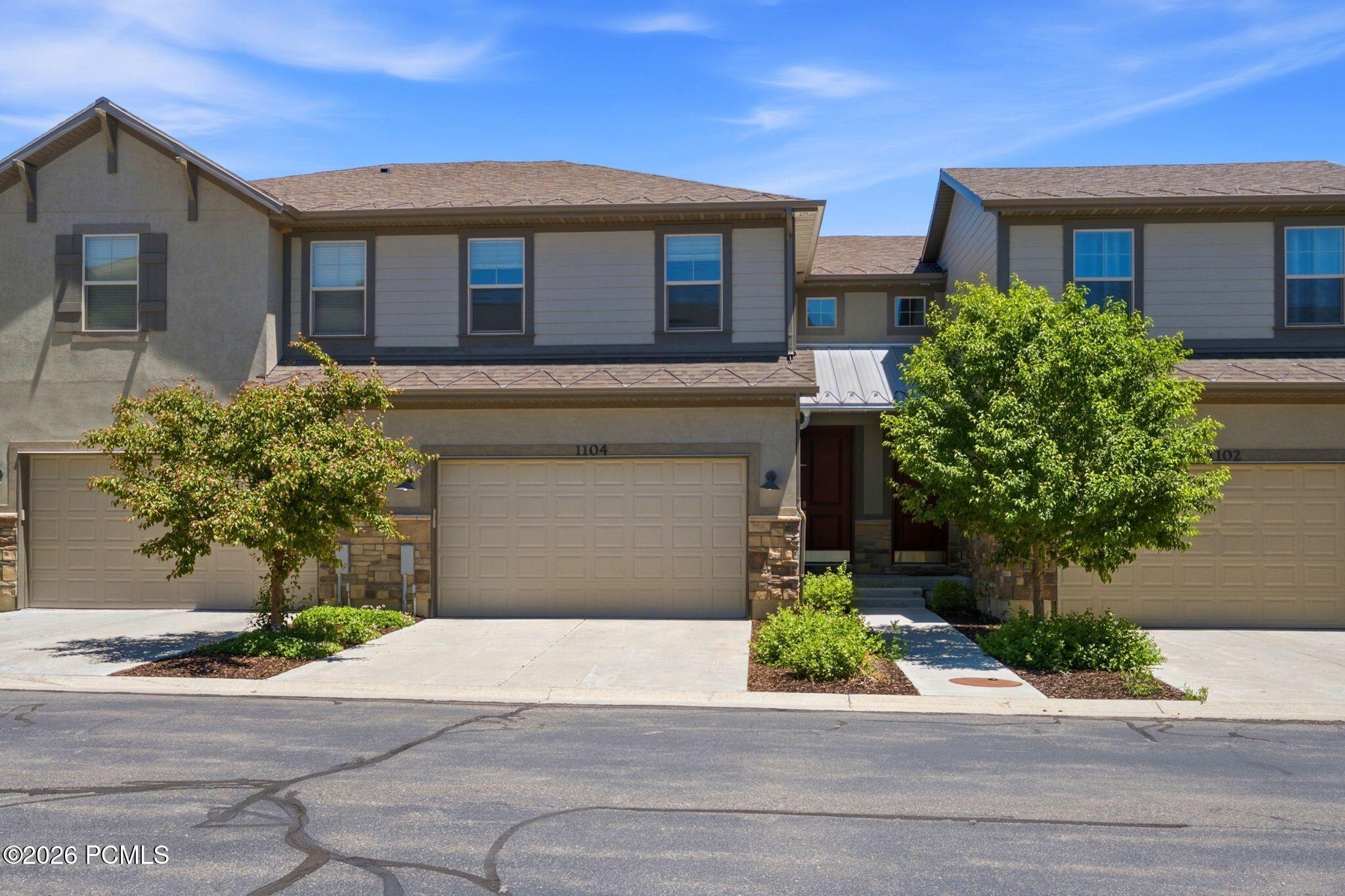 Contemporary townhome exterior featuring a stucco and siding facade, stone accents, two integrated garages with overhead doors, an inviting front entry, and established landscaping